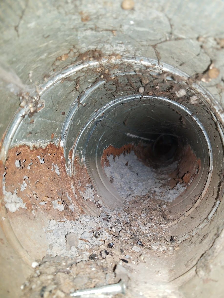 Close-up of a rusty metal pipe opening with corrosion and debris inside