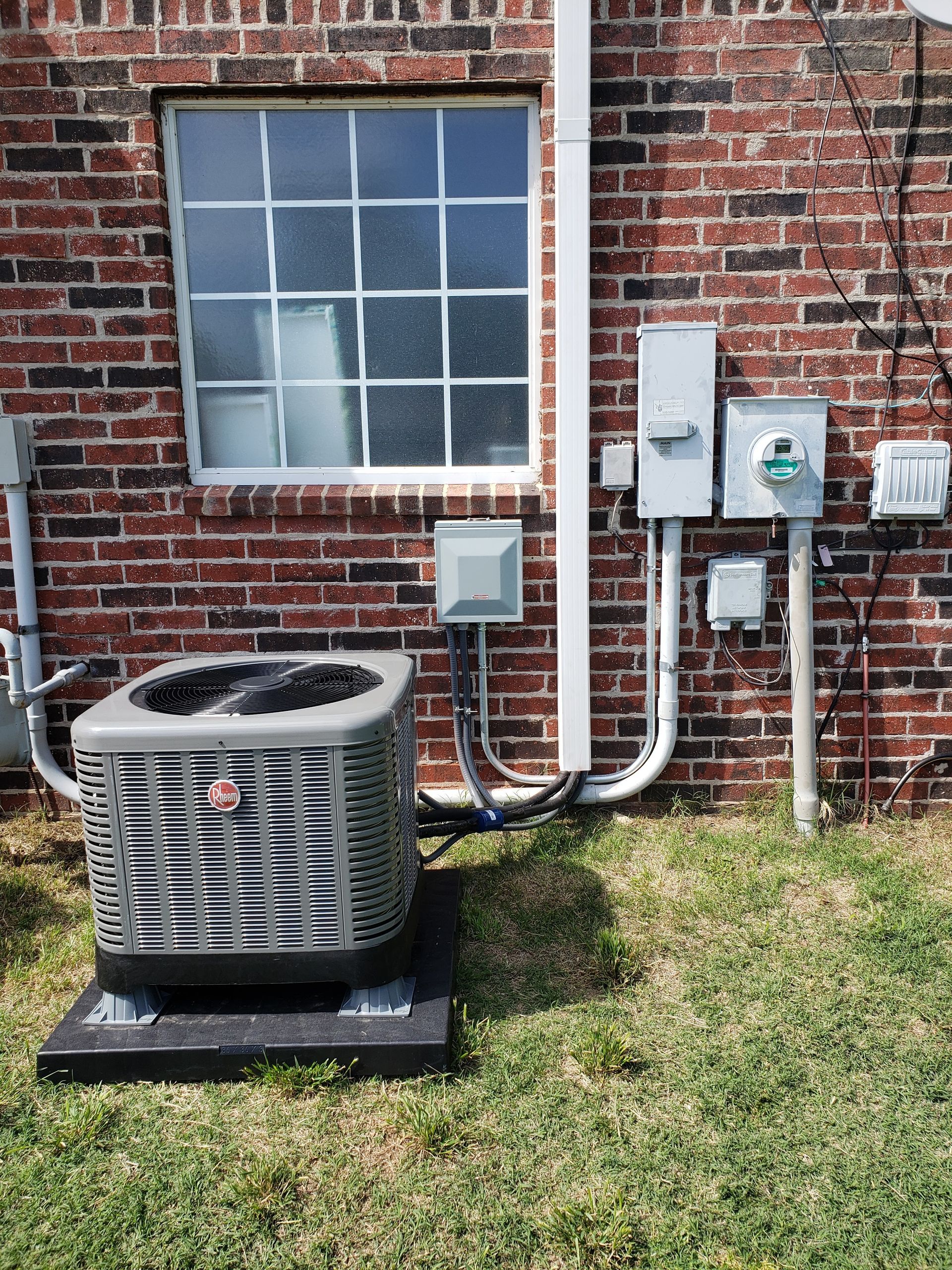 Outdoor HVAC unit beside a brick building wall with a window and utility meters