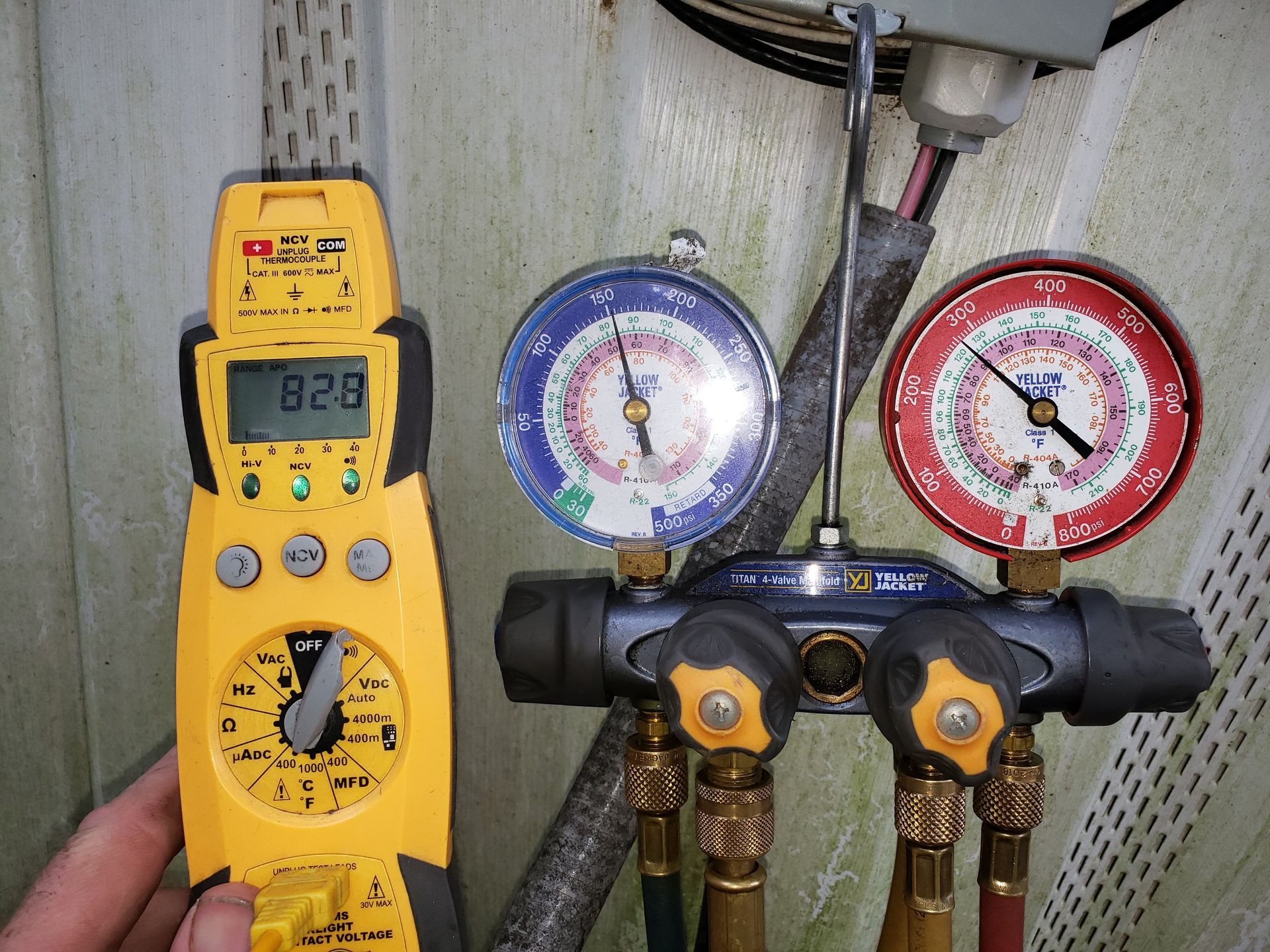 Yellow digital meter beside blue and red HVAC manifold gauges on copper pipes in a mechanical setting