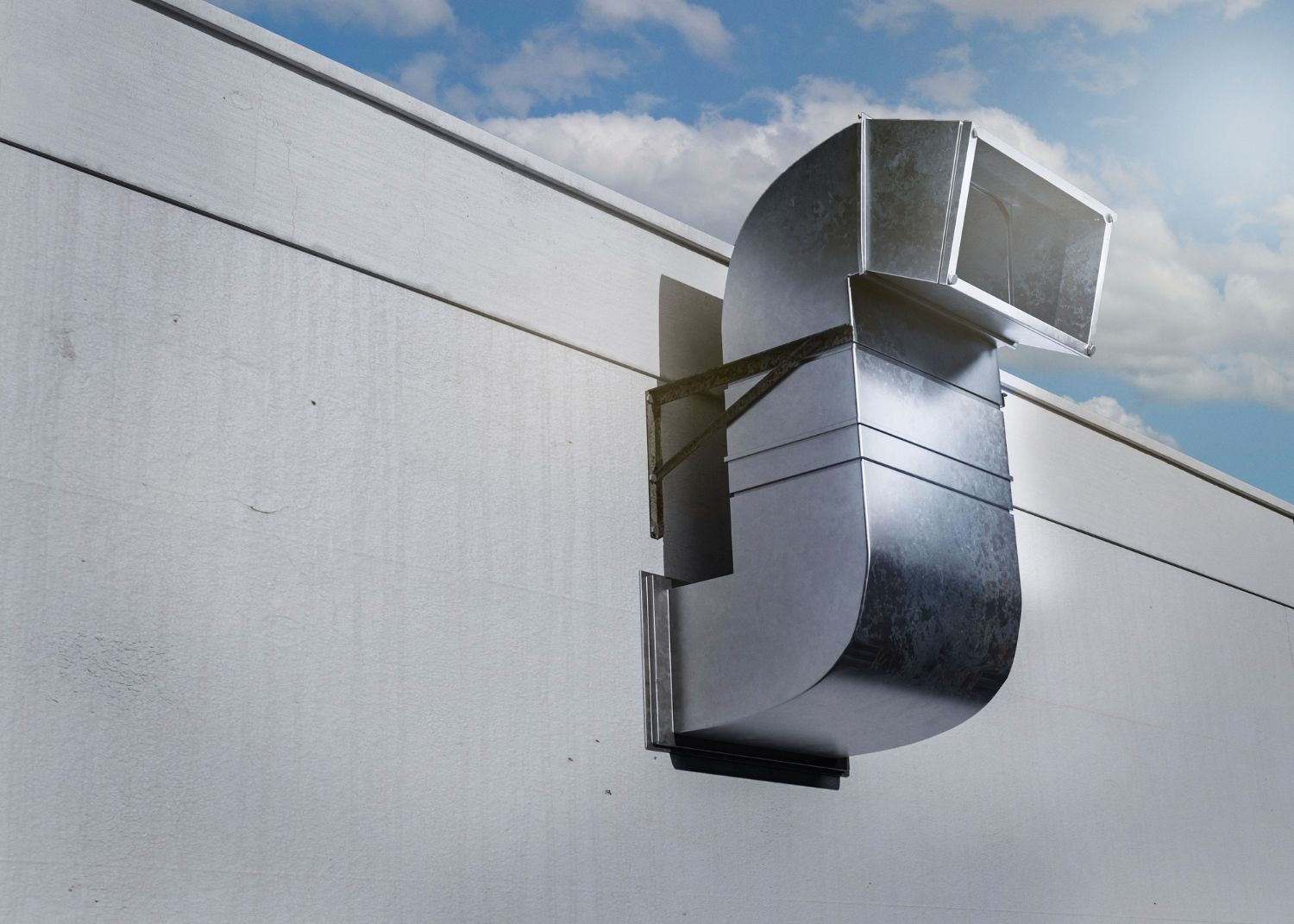 Metal HVAC vent on a white wall under a blue sky