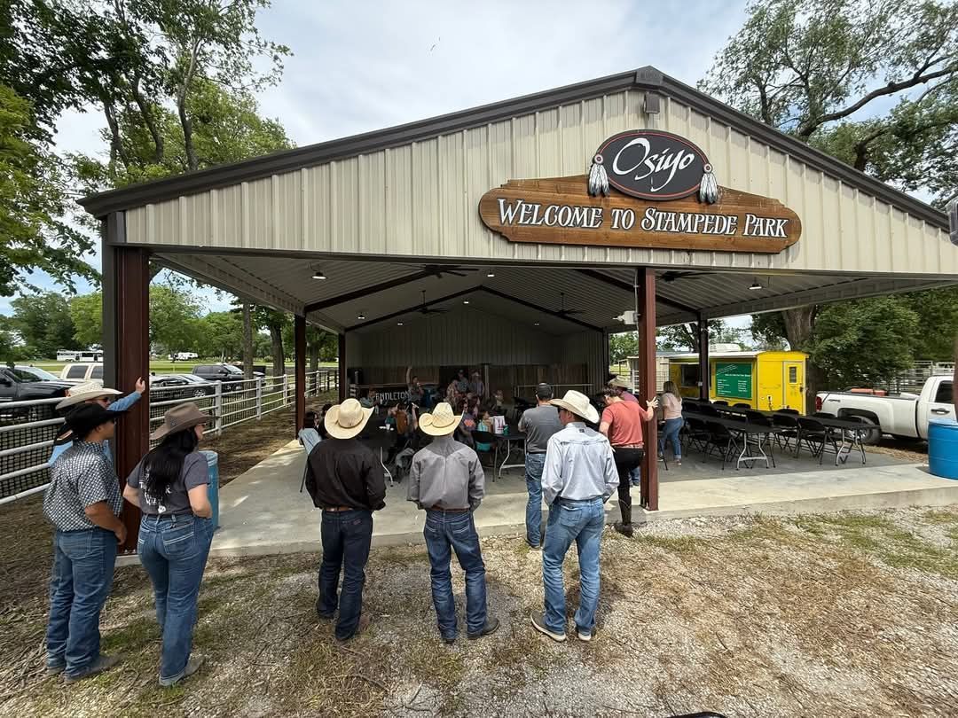 People in cowboy hats gathered outside a covered pavilion with farm equipment and signage.