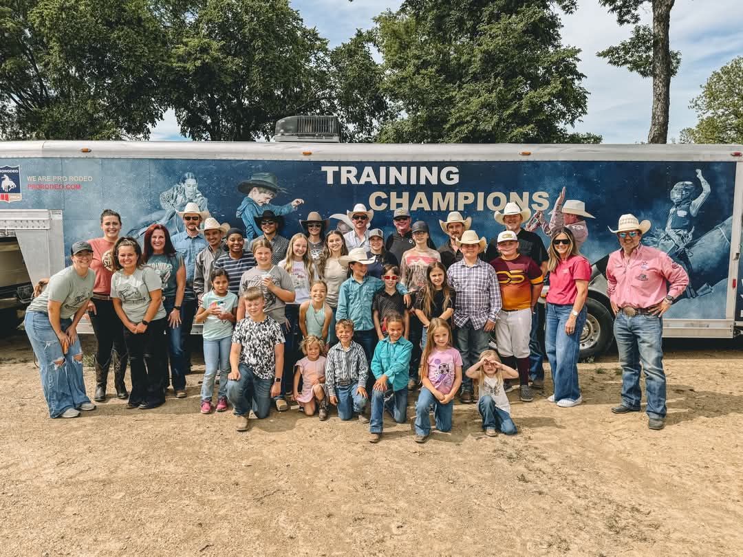 Group posing in front of a blue “Training Champions” trailer at an outdoor event.