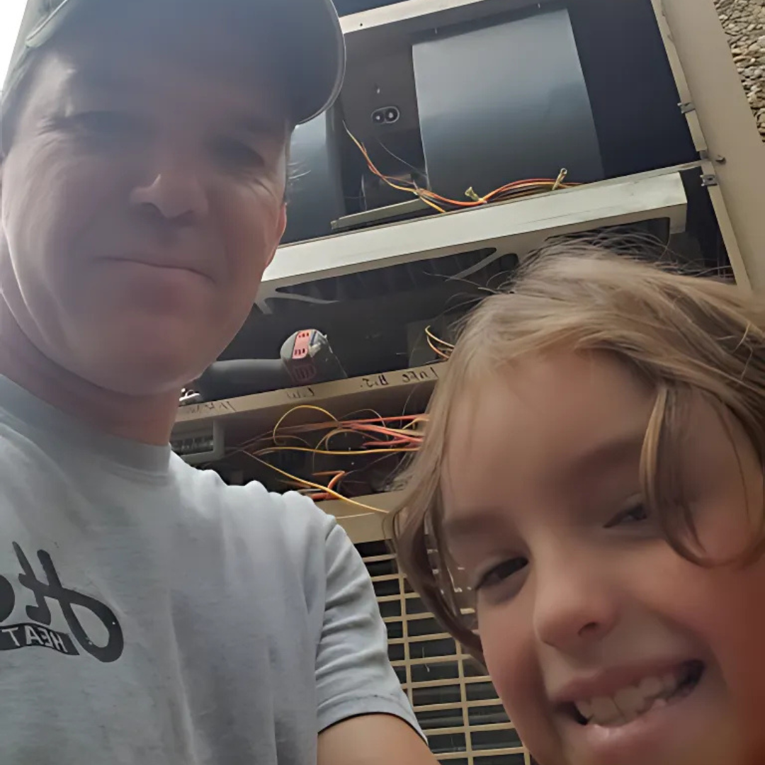 Smiling man and child in front of open electronics cabinet with wires and equipment