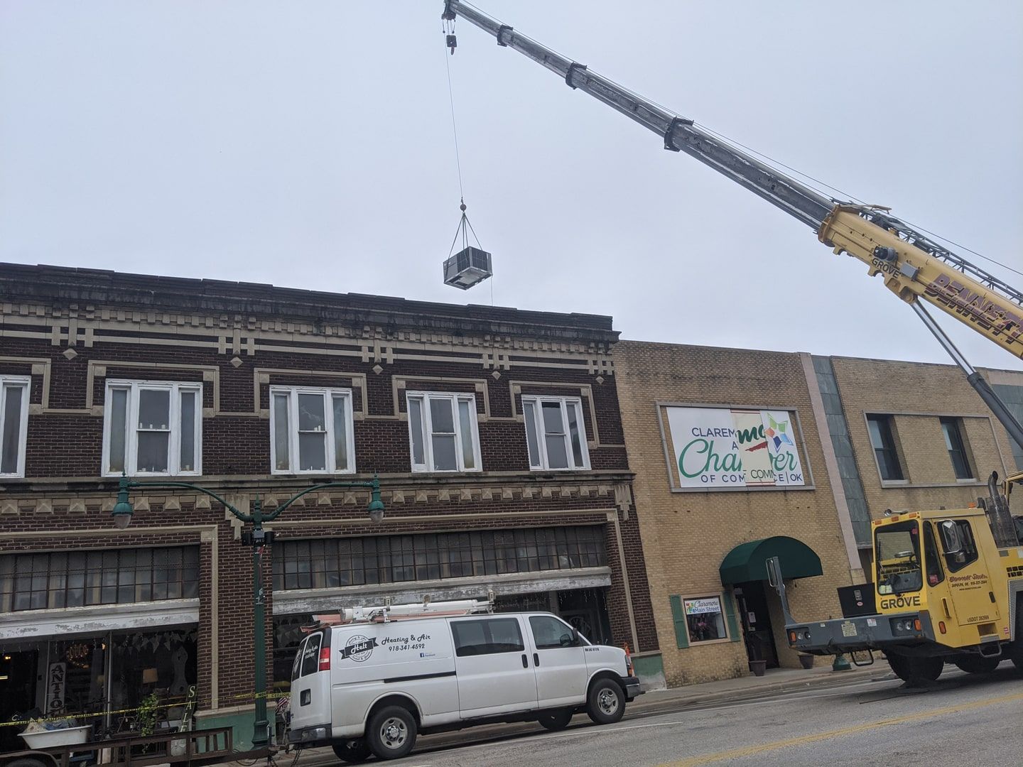 Crane lifting a load beside a row of old storefronts, with a white van parked below.