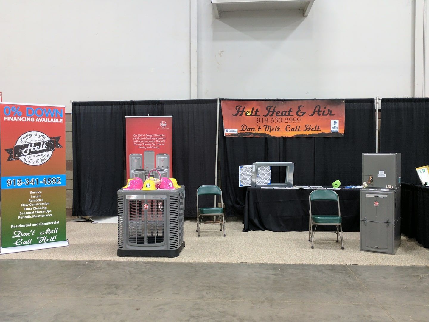 Indoor vendor booth with orange banner, black backdrop, chairs, table, and colorful display stands