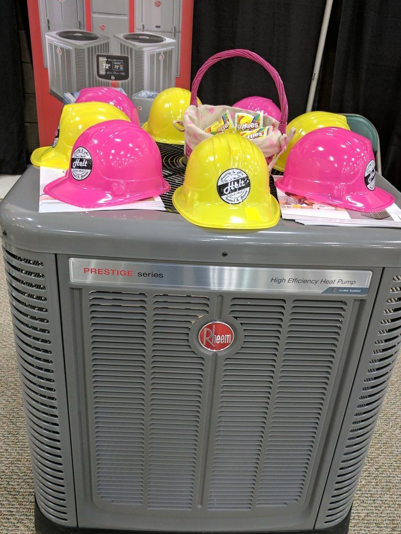 Three colorful hard hats on top of a gray HVAC unit, with a pink basket in the background.