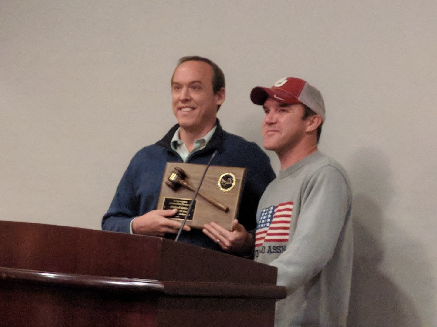 Two men stand behind a podium holding a plaque and smiling during a presentation.