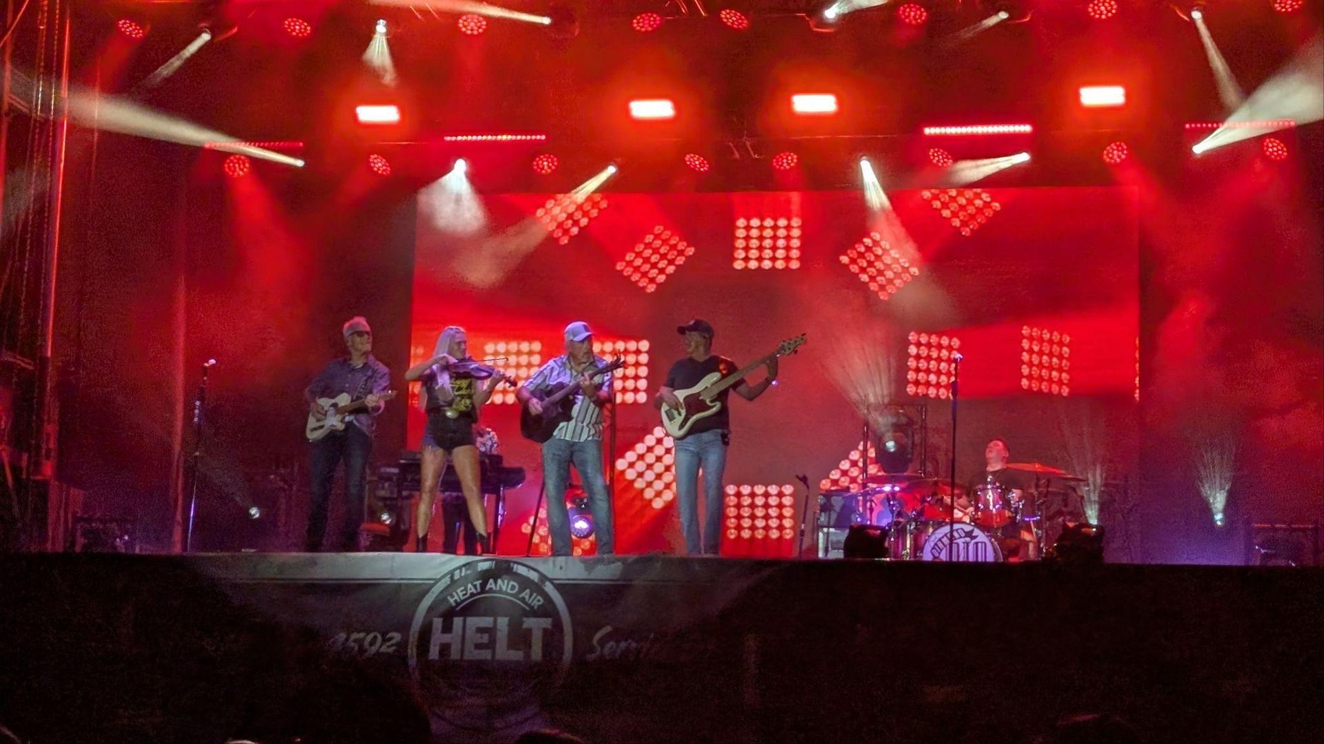 Rock band performing on stage under red lights and spotlights