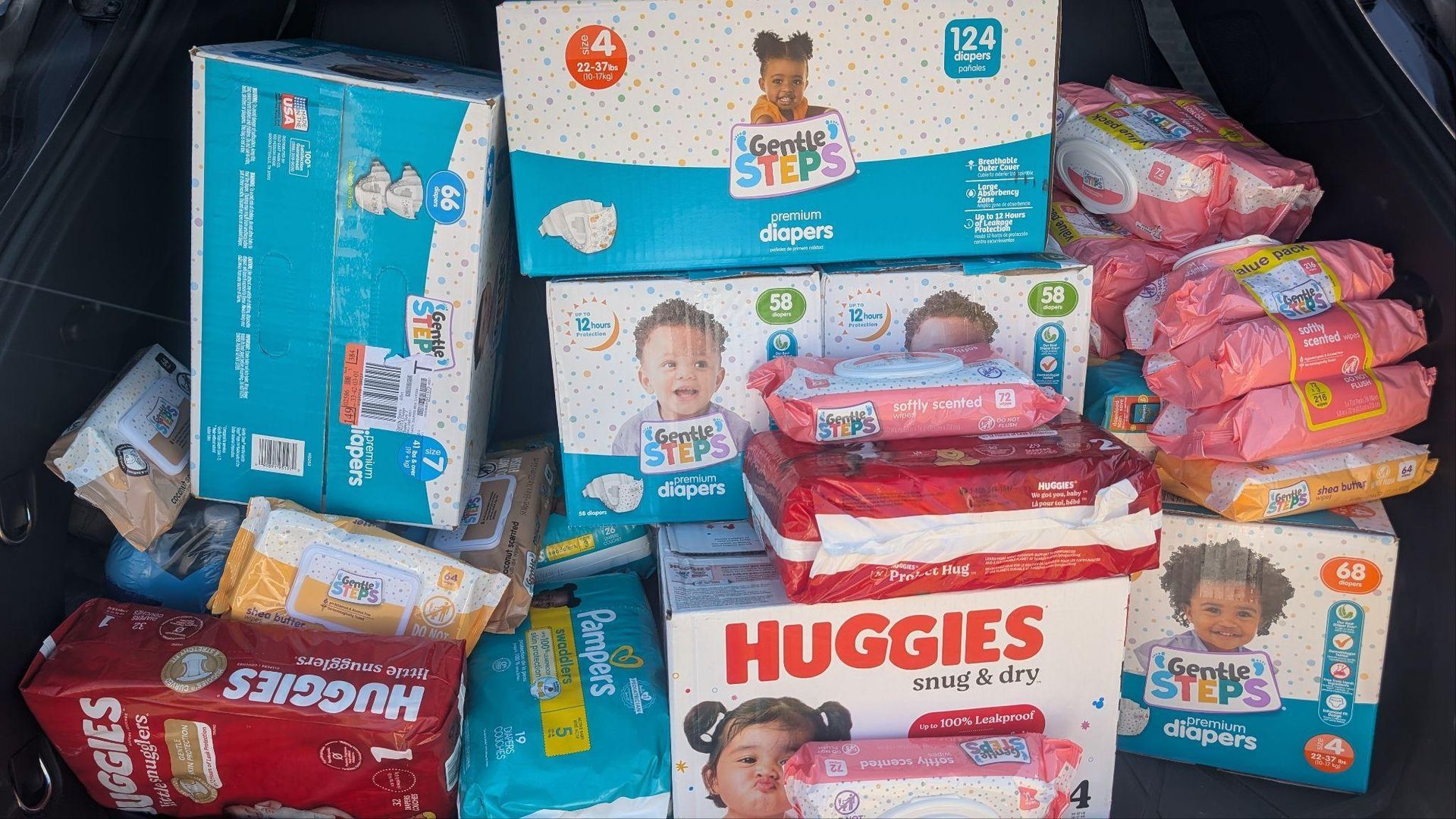 Assorted Huggies and other diaper packs stacked in a pile on a store shelf.