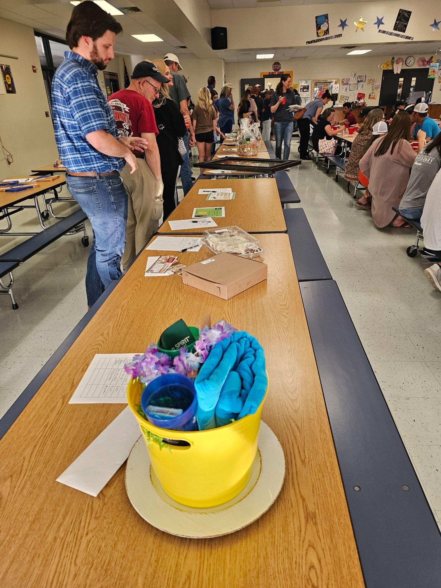 Yellow bucket of colorful items on a table at a community event, with people gathered around in a hall