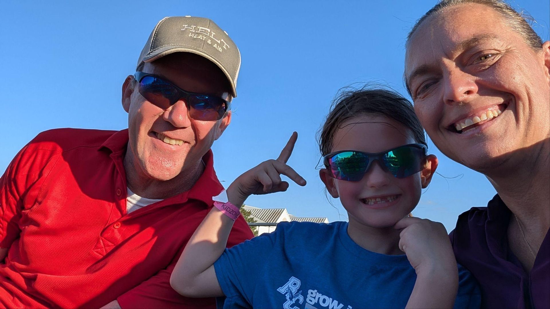 Three smiling people outdoors in bright sun, posing for a selfie on a boat or dock.