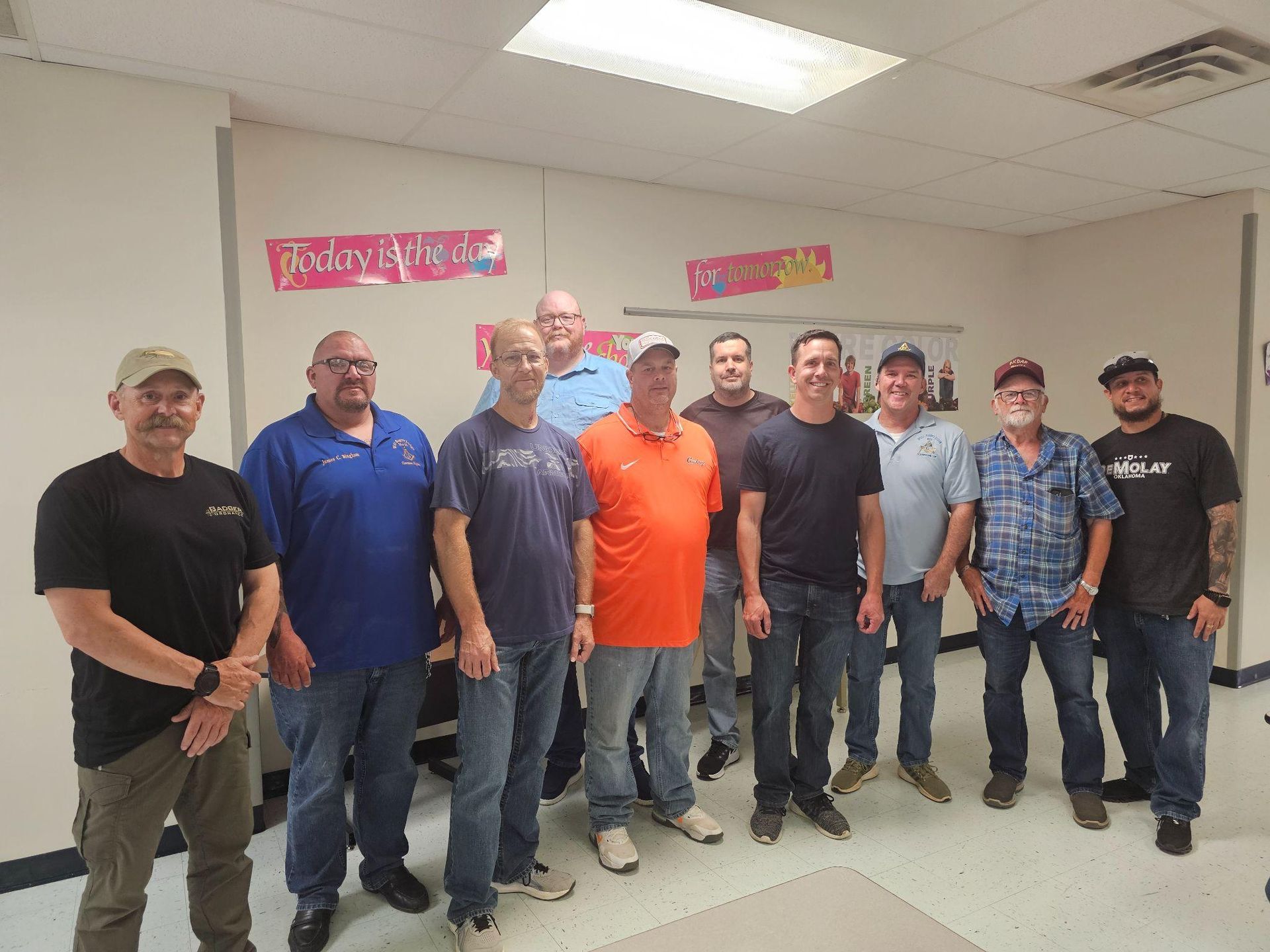 Group of men standing together indoors in a room, posing for a photo under bright ceiling lights.