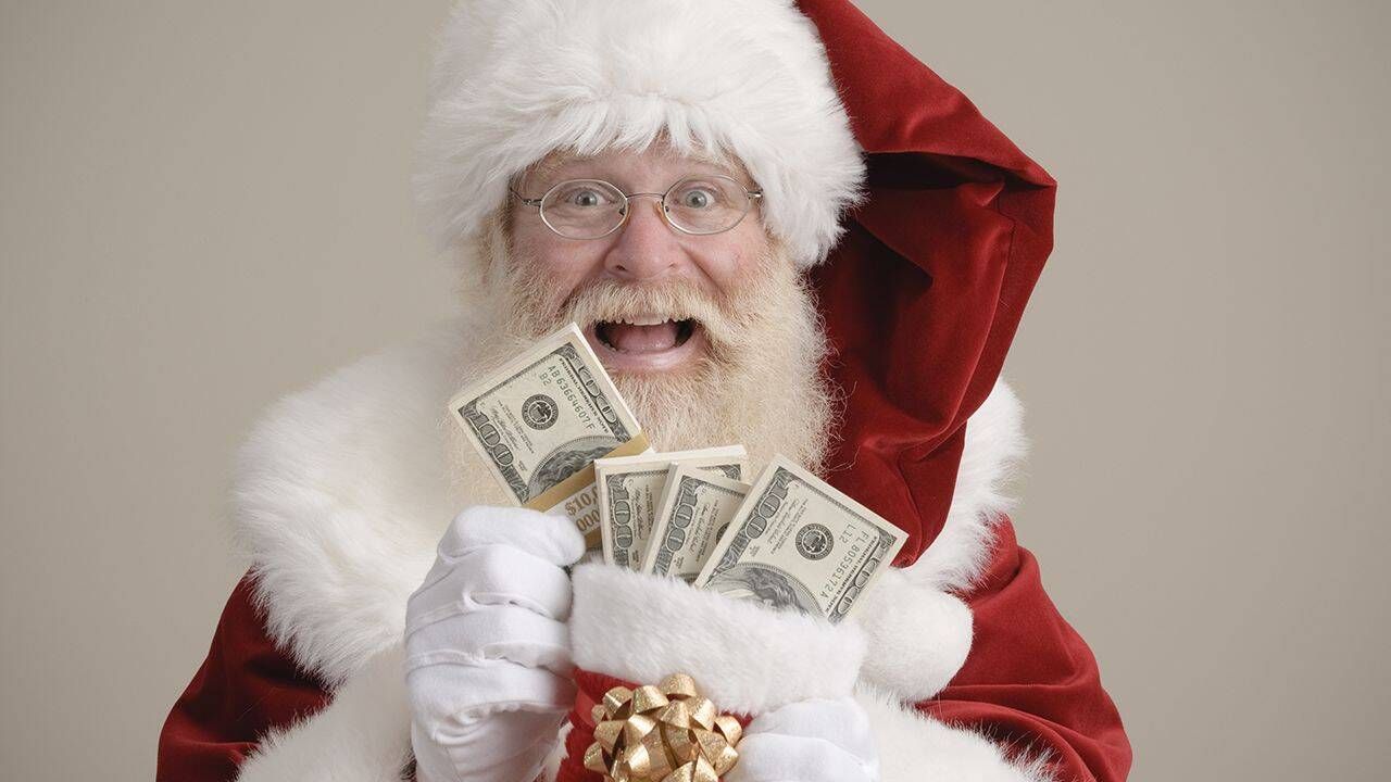 Santa in red suit holding cash and a gift box against a plain background