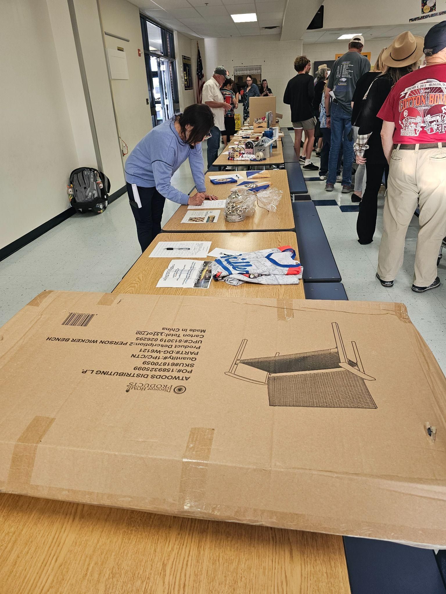 People browsing informational tables in a hallway, with a large cardboard box in the foreground.