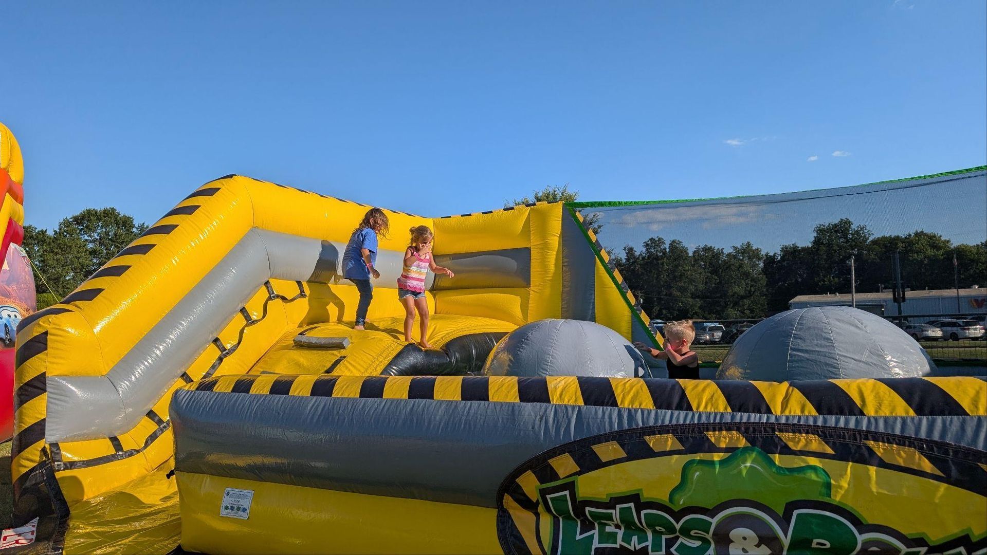 Children on a yellow inflatable obstacle course outdoors under a clear blue sky