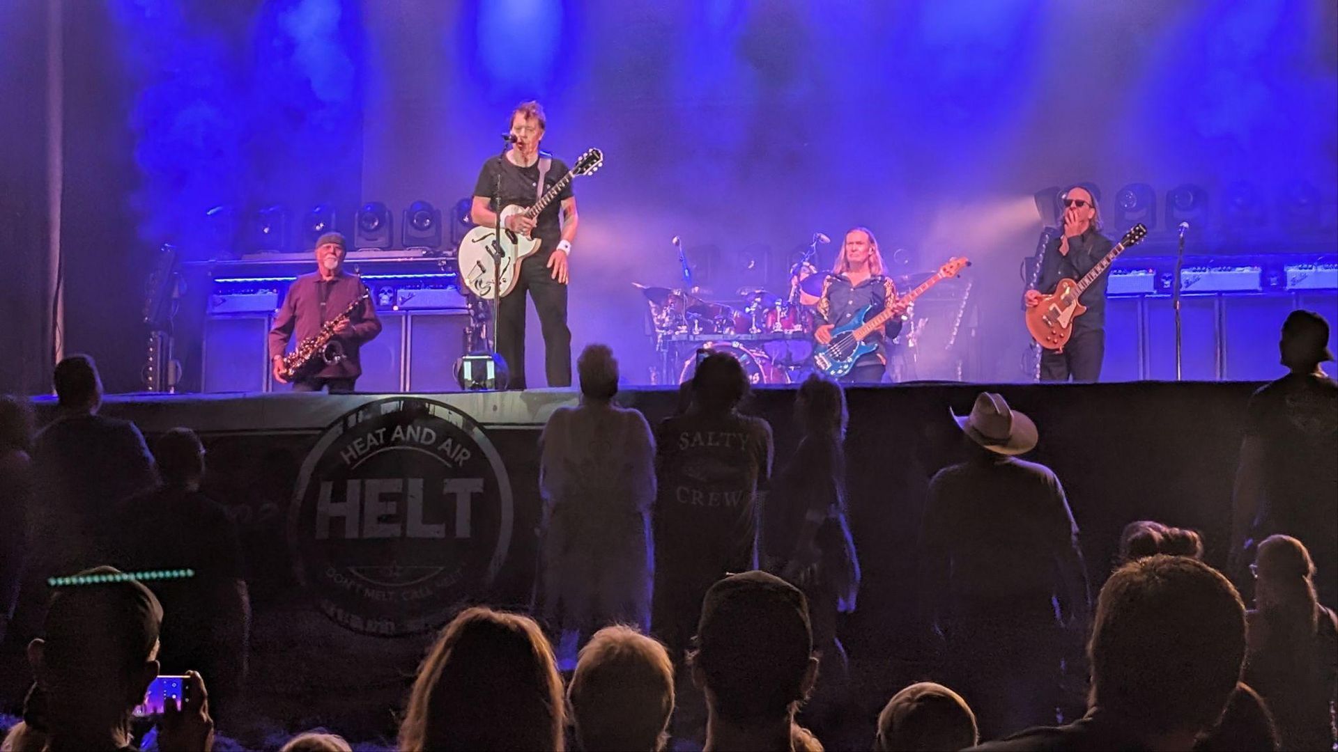Band performs on a blue-lit stage with a crowd silhouetted in front.