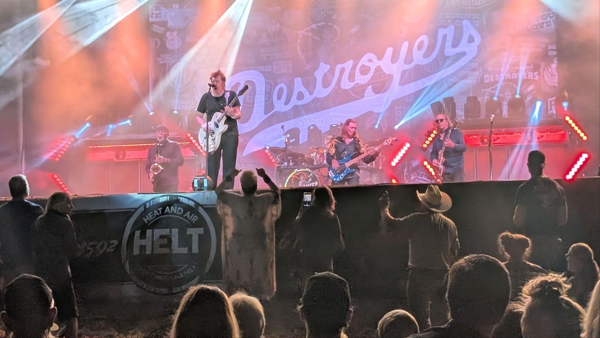 Singer performing on an outdoor stage with pink lights, crowd in front, and “Discover” banner in back