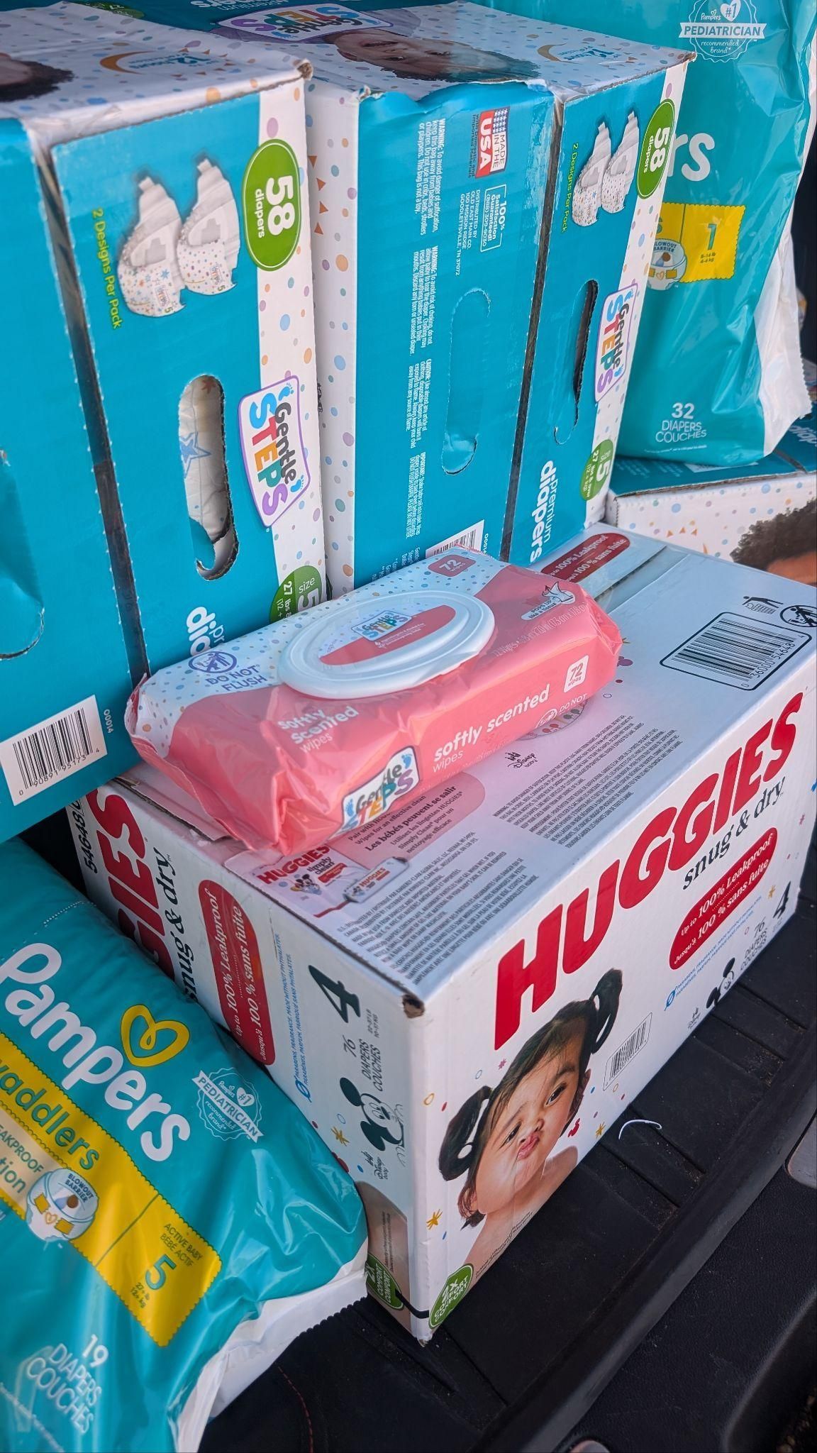 Boxes of Huggies diapers and wipes stacked on a store shelf, with a pink package on top.
