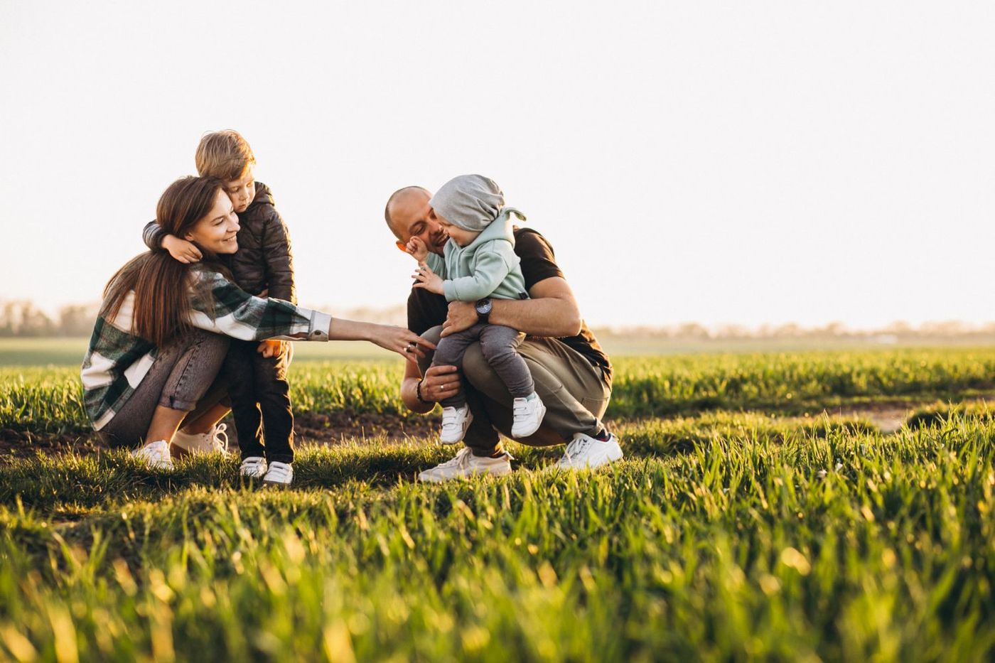 Family kneeling in a grassy field, laughing and hugging in warm sunlight