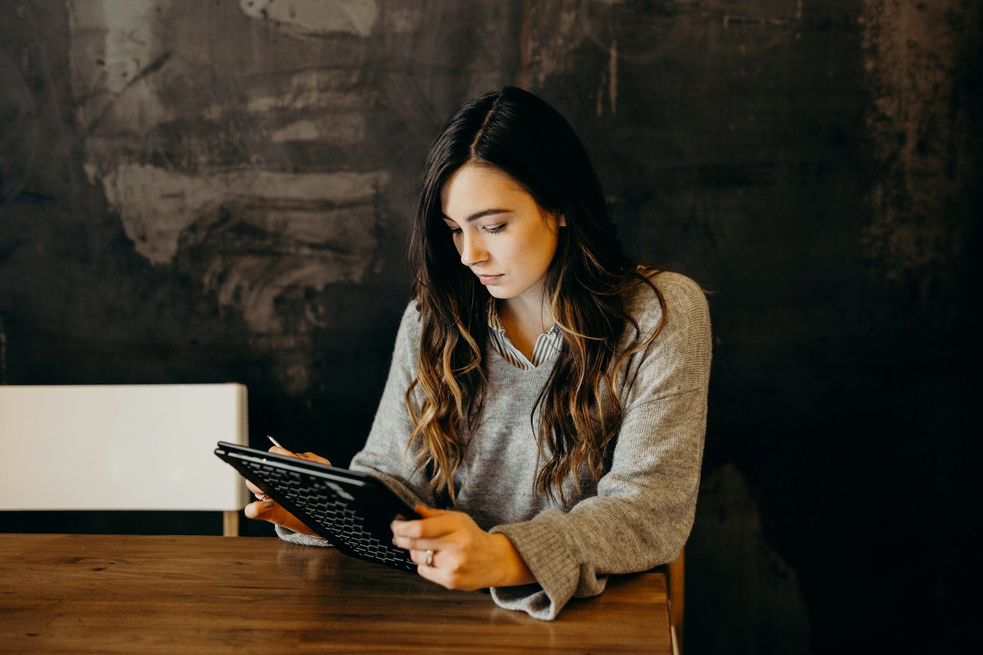 Woman writing in a notebook at a wooden table against a dark wall.