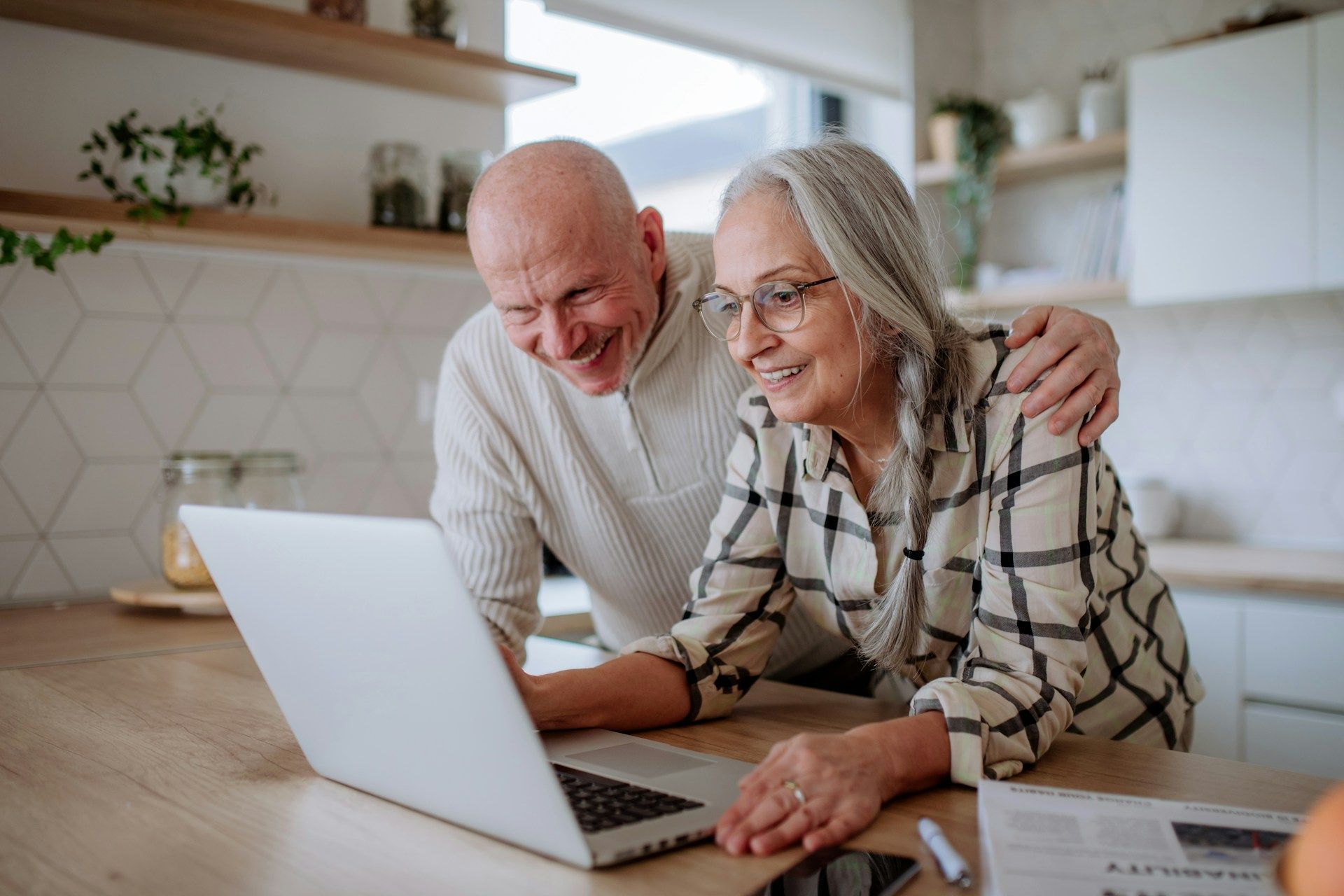 Two people smiling and using a laptop at a kitchen table