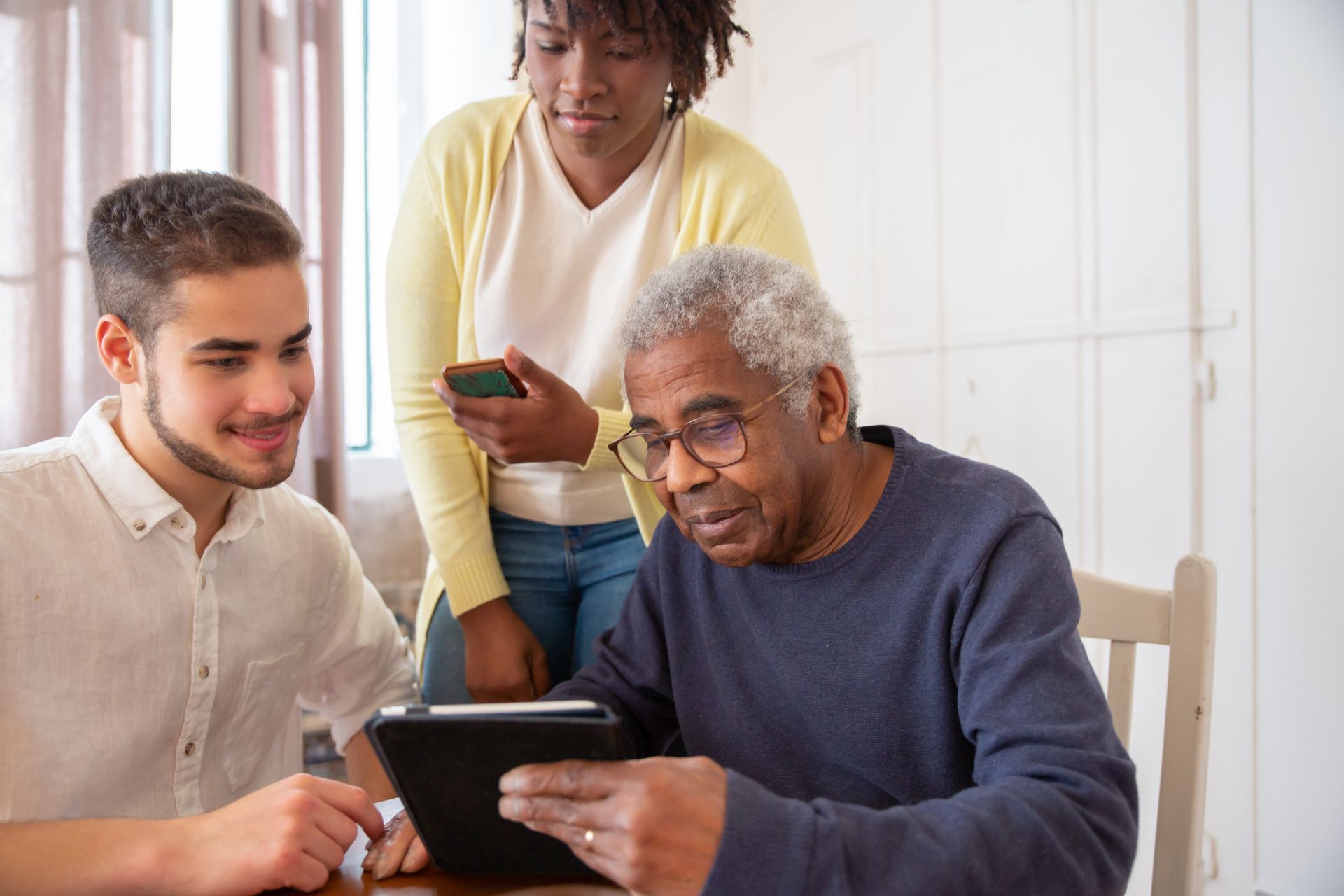 Three people gathered around a tablet, smiling and looking at the screen in a bright room