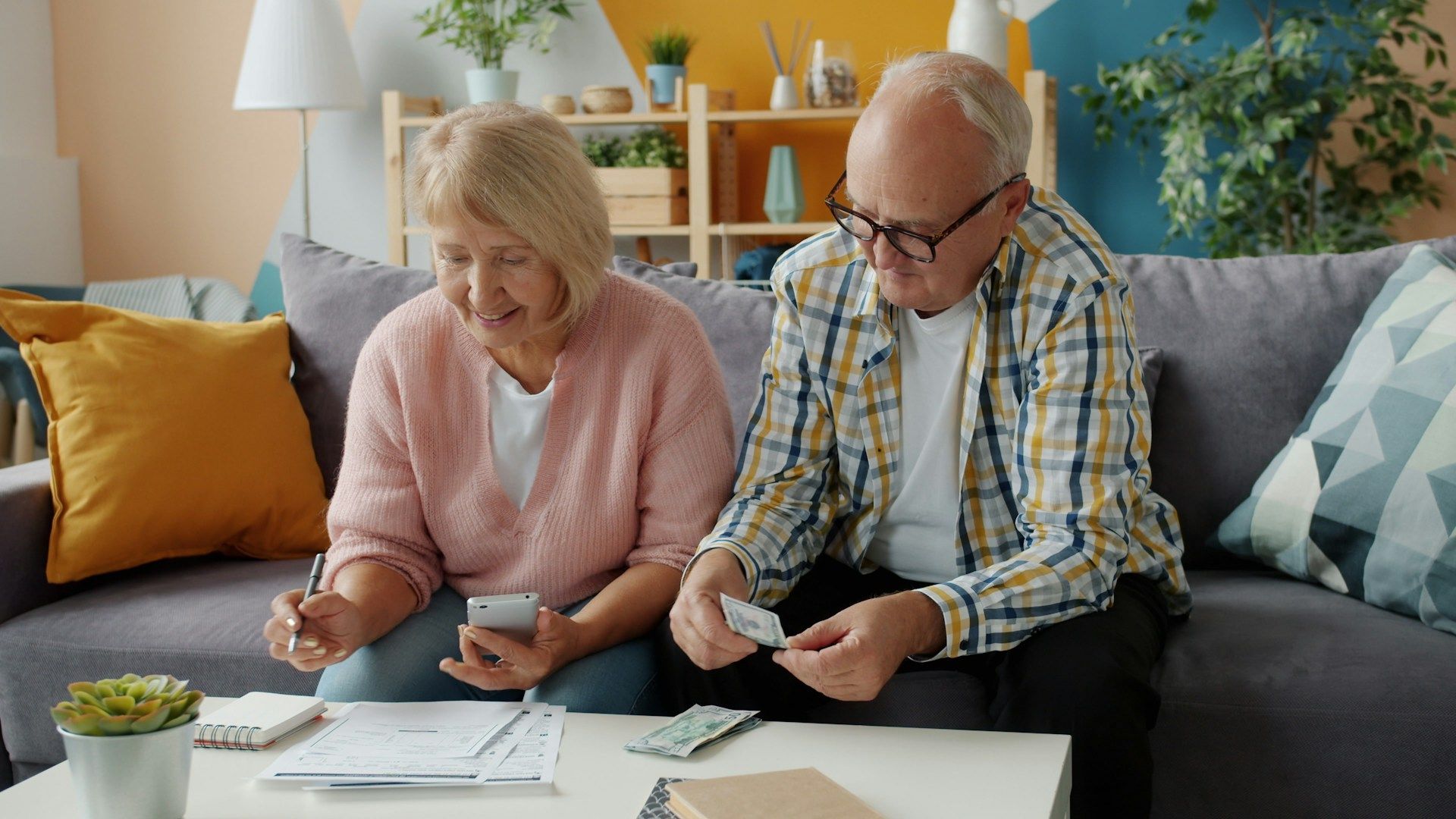 Two people reviewing documents on a couch in a bright living room with a laptop and coffee table