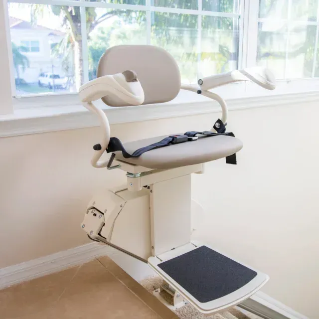Stairlift with a seat and attached basket holding groceries on a staircase near a wooden door.