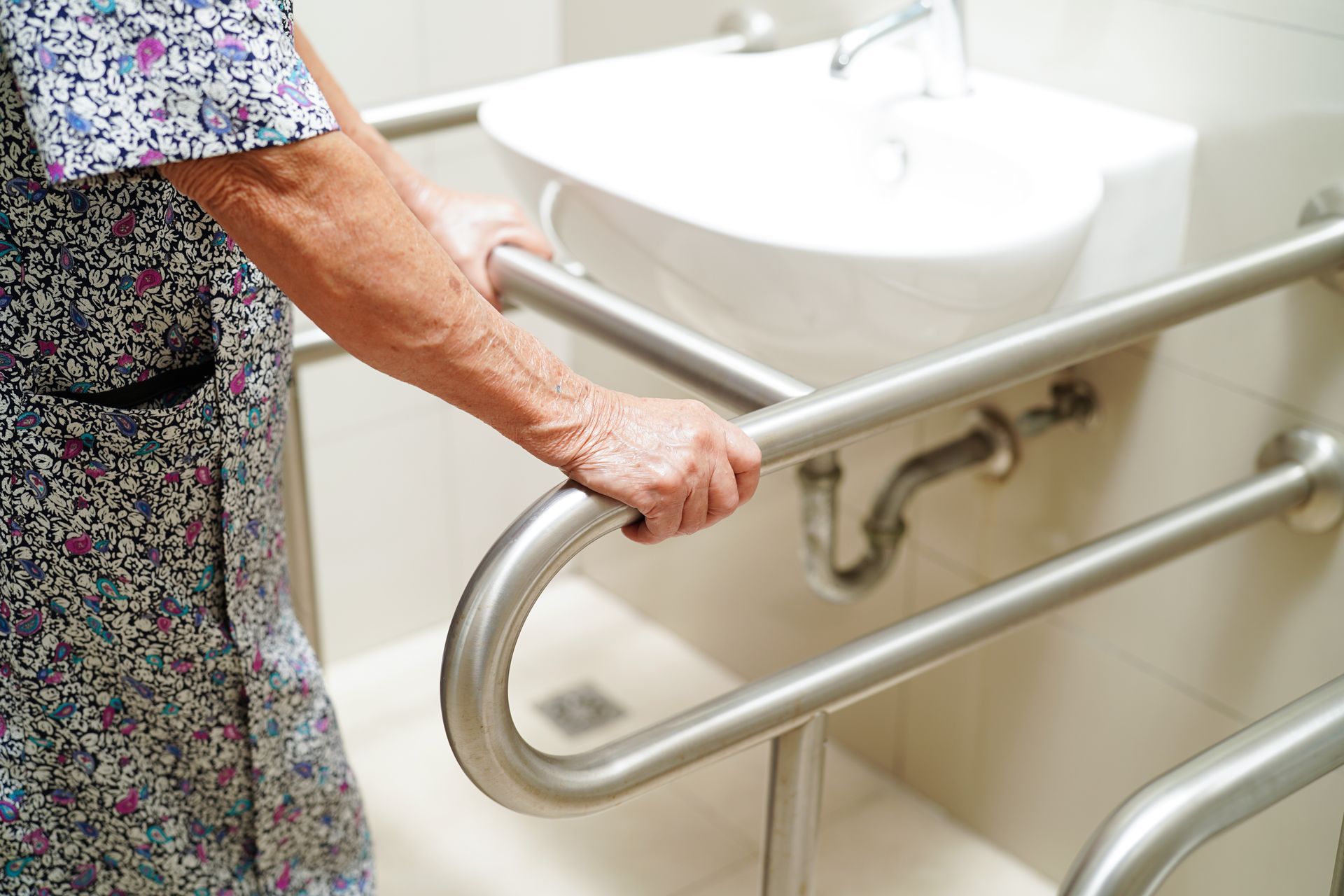 An elderly woman is holding onto a hand rail in a bathroom.