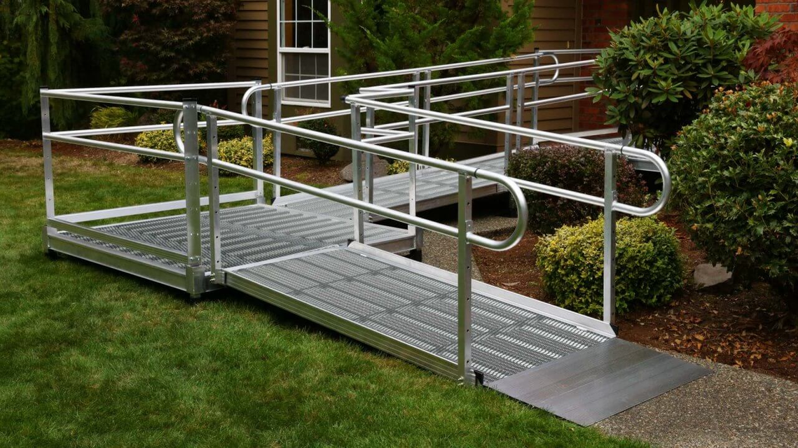 Aluminum wheelchair ramp with handrails in a yard leading to a house.