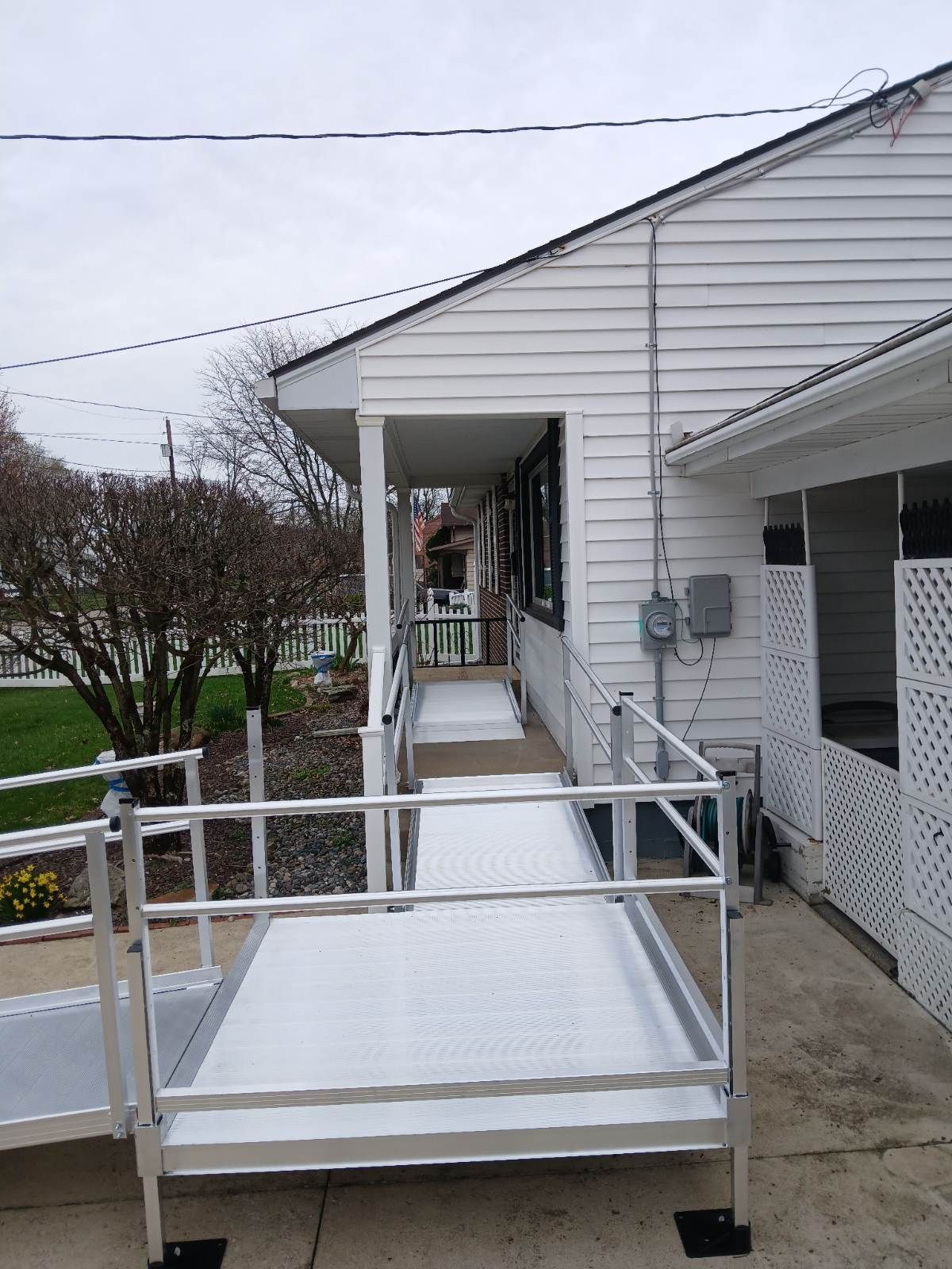 Aluminum wheelchair ramp leading up to a white building with a covered porch. Gray overcast sky.