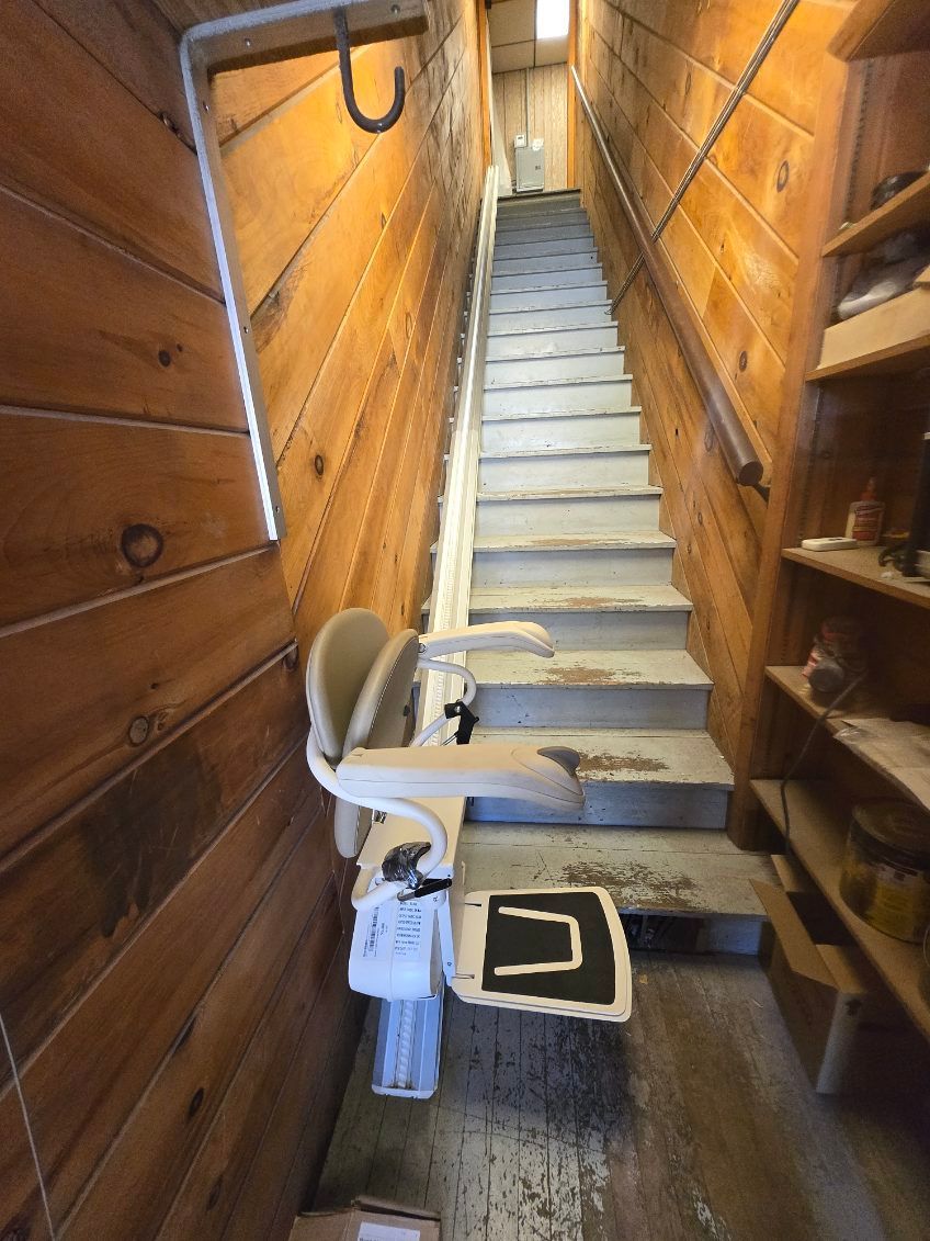 Narrow staircase with a stairlift, flanked by wood paneling and shelves.