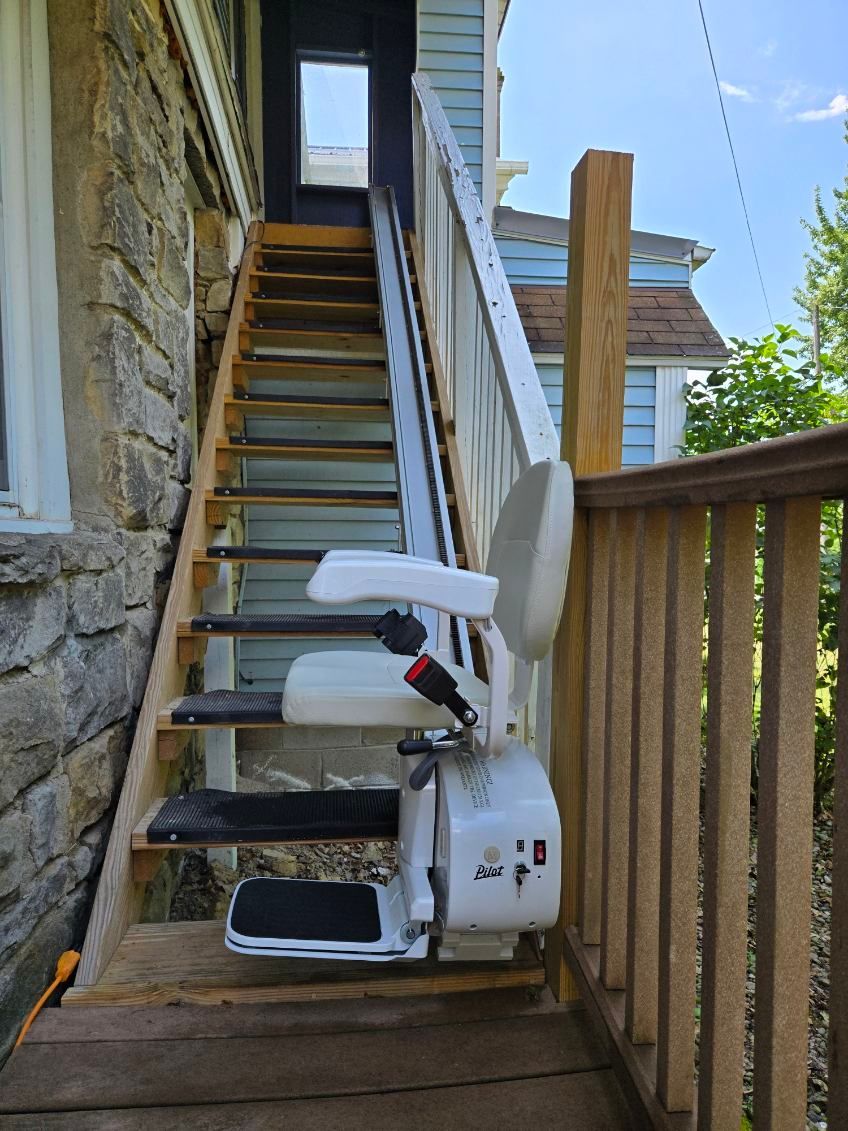 Stair lift installed on an outdoor wooden staircase, offering accessibility. White chair ascends steps.
