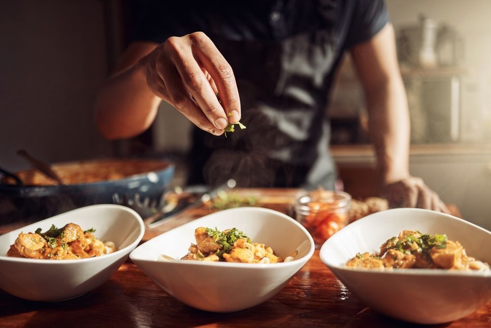 Person Sprinkles Green Herbs on Three Bowls of Chicken and Rice — Chefs2Go in Mackay, QLD