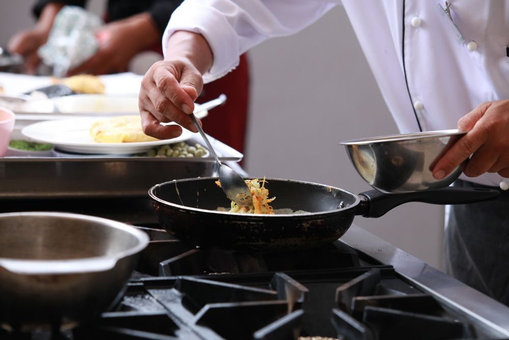 Chef Cooking Food in a Pan on a Stove, Using a Spoon to Stir Ingredients — Chefs2Go in Airlie Beach, QLD