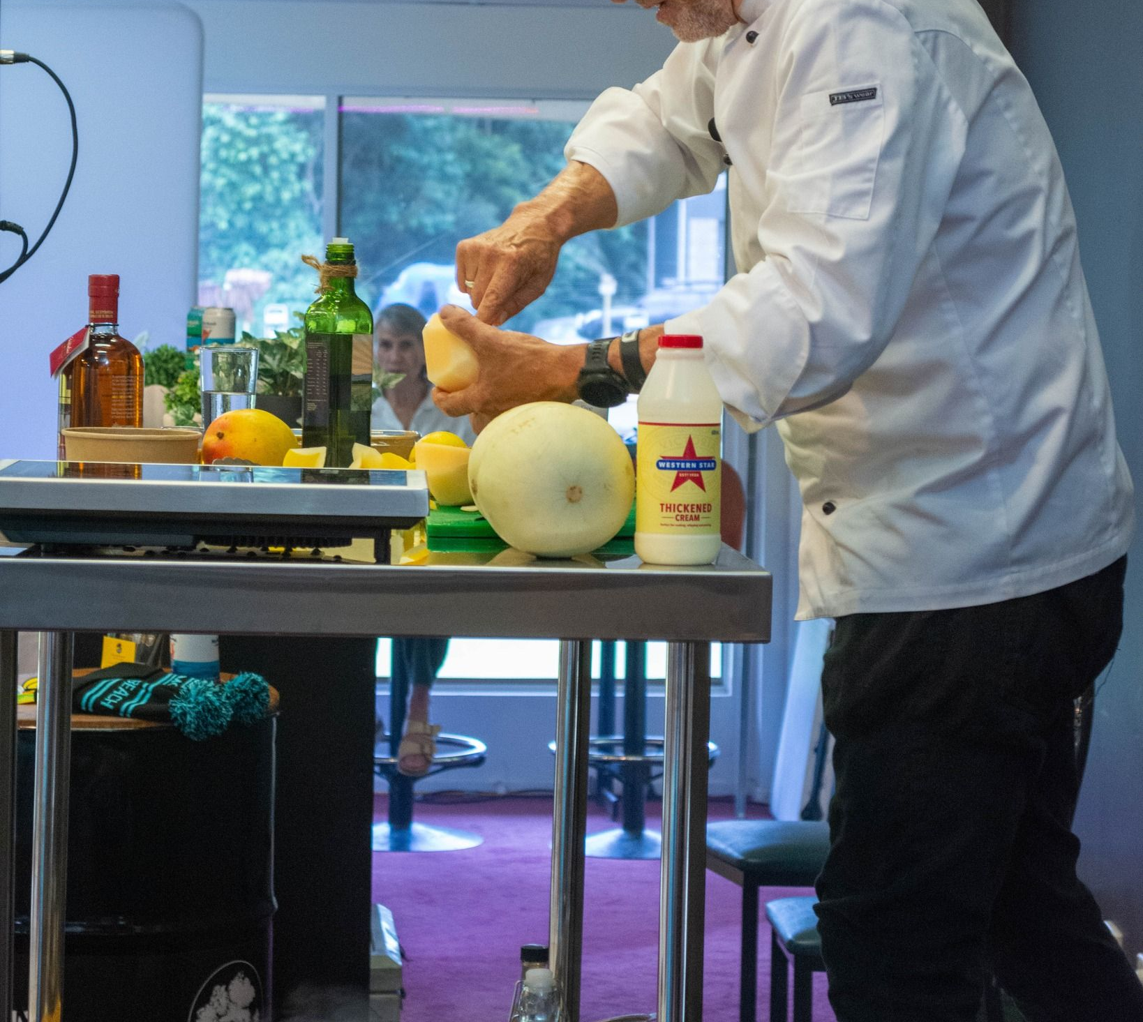 Chef in White Coat and Black Cap, Peeling a Melon at a Countertop Station — Chefs2Go in Rockhampton, QLD