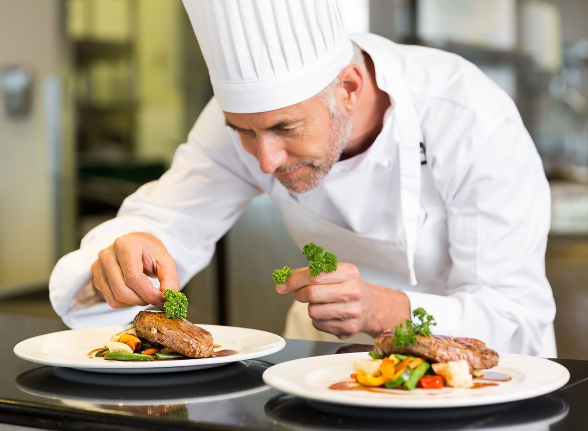 Chef in White Uniform Garnishing Plates of Food With Parsley in a Restaurant — Chefs2Go in Darwin, NT