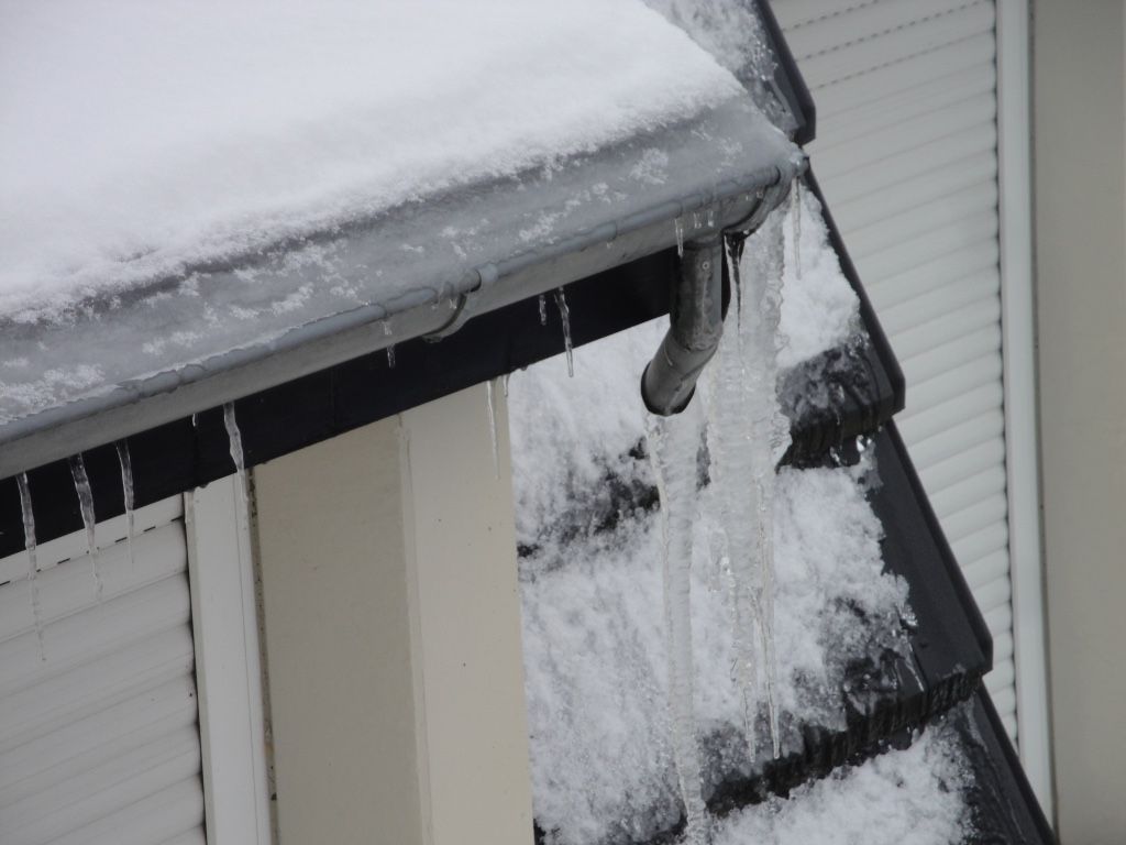 Une gouttière avec de la neige dessus et des glaçons qui y pendent.