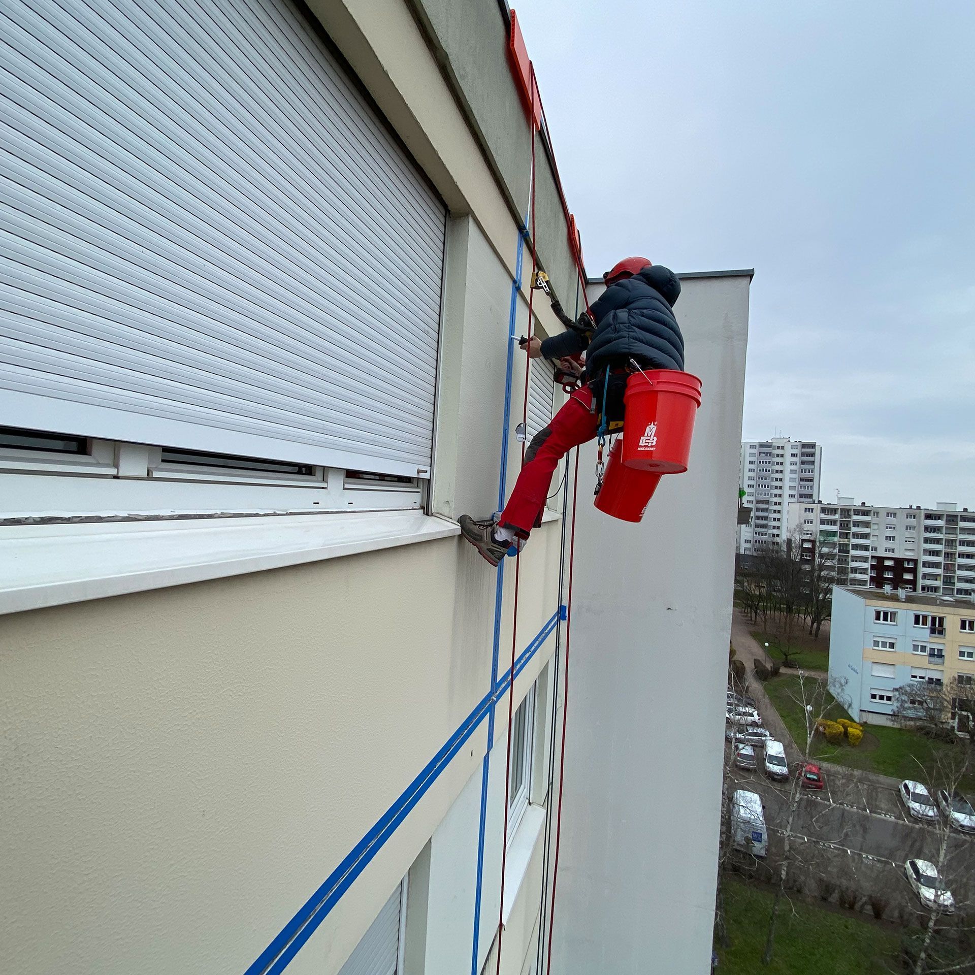 Un homme avec un seau rouge sur le dos escalade un bâtiment