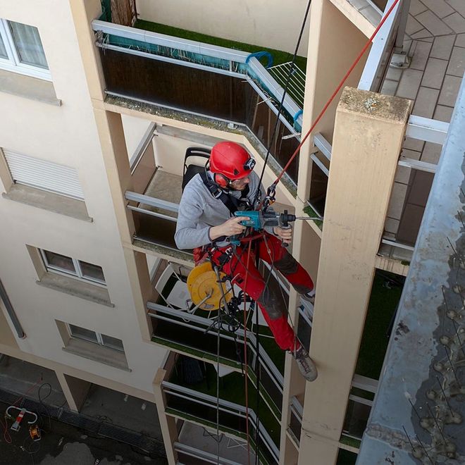 Un homme portant un casque rouge travaille sur le balcon d'un immeuble