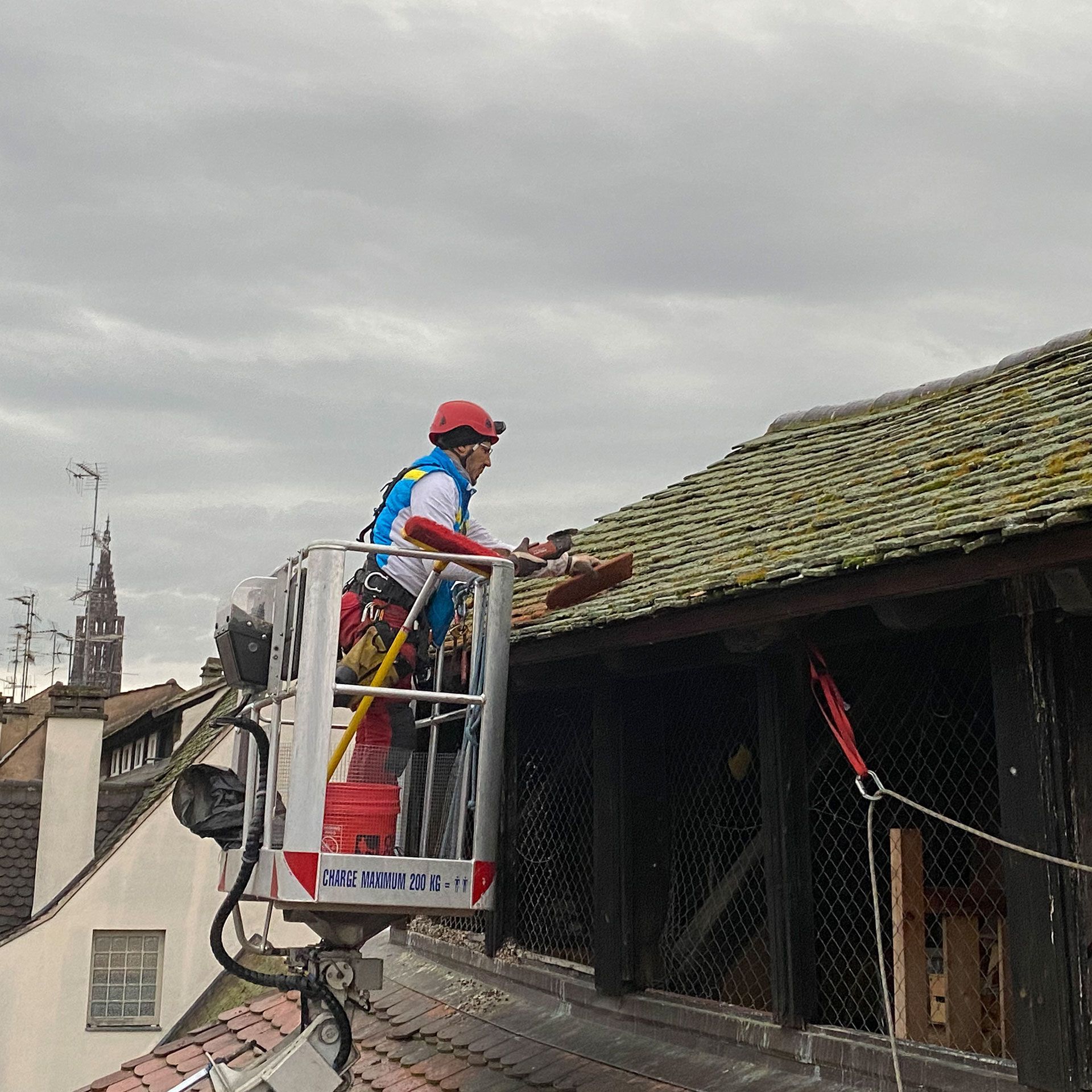 Un homme se tient debout dans un seau au sommet d'un toit.