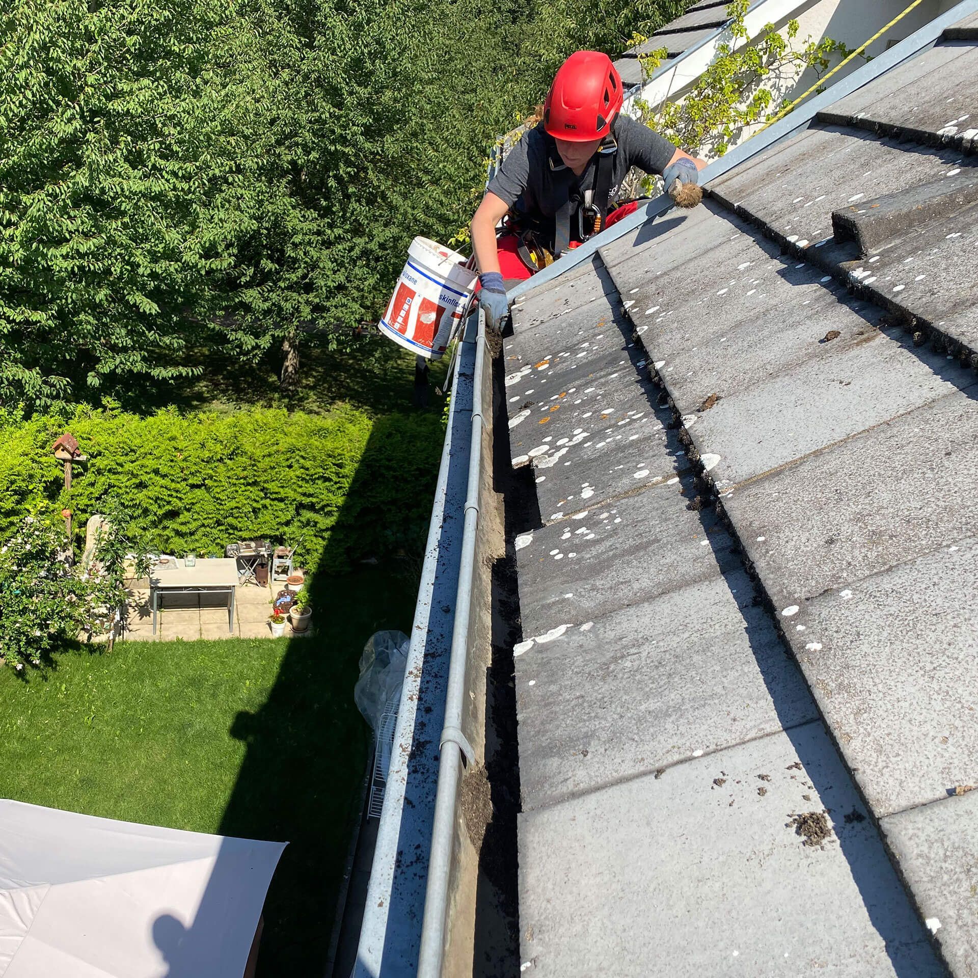 Un homme portant un casque rouge nettoie une gouttière sur un toit