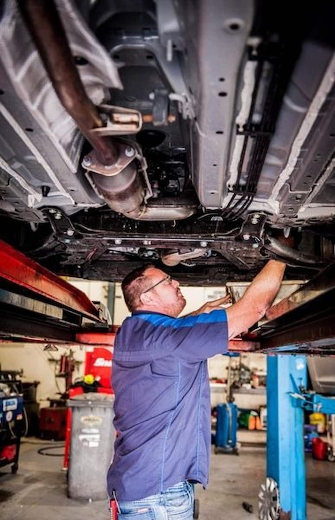 Mechanic Works Under a Car Lifted on A Hoist — DK Mechanical Repairs in Warners Bay, NSW