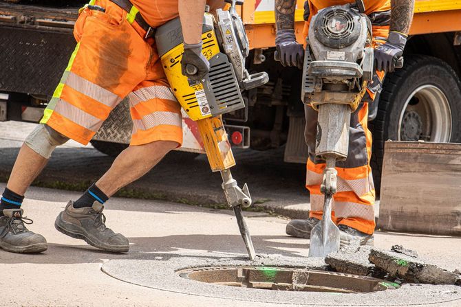 Worker in red hard hat opening a manhole cover in a grassy area