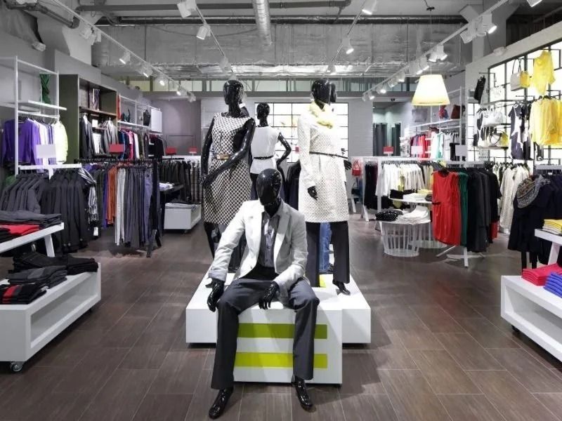 En una tienda de ropa, unos maniquíes exhiben conjuntos en blanco y negro alrededor de una modelo sentada sobre un pedestal.