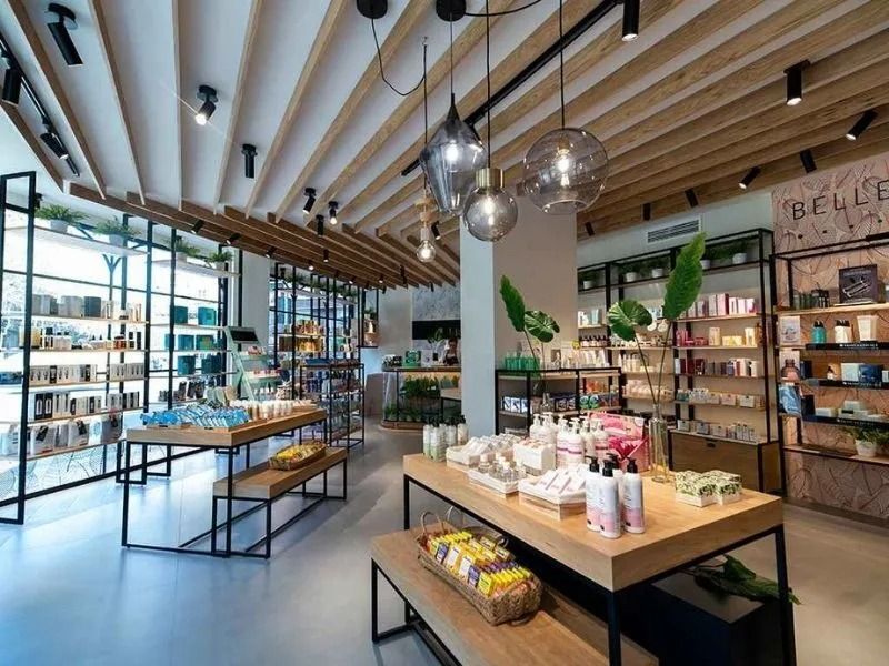 Interior de una boutique moderna con estanterías de madera, lámparas colgantes y mesas de exposición de productos.