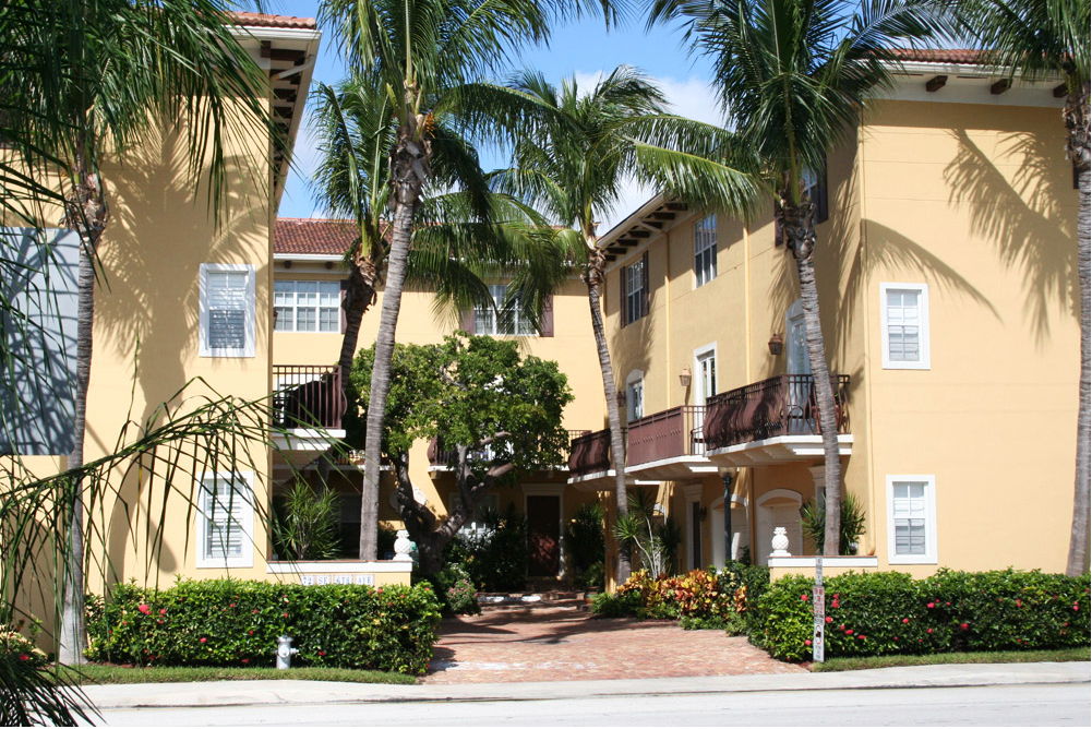 Yellow stucco townhouses with palm trees and a brick pathway.
