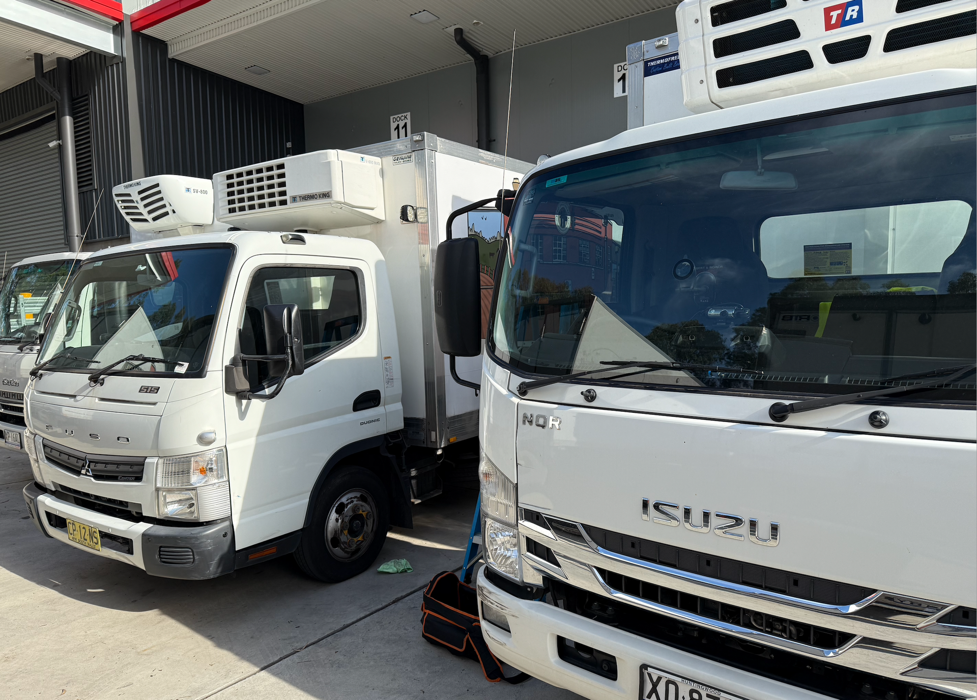 Two white Isuzu refrigerated trucks parked side-by-side at a loading bay.