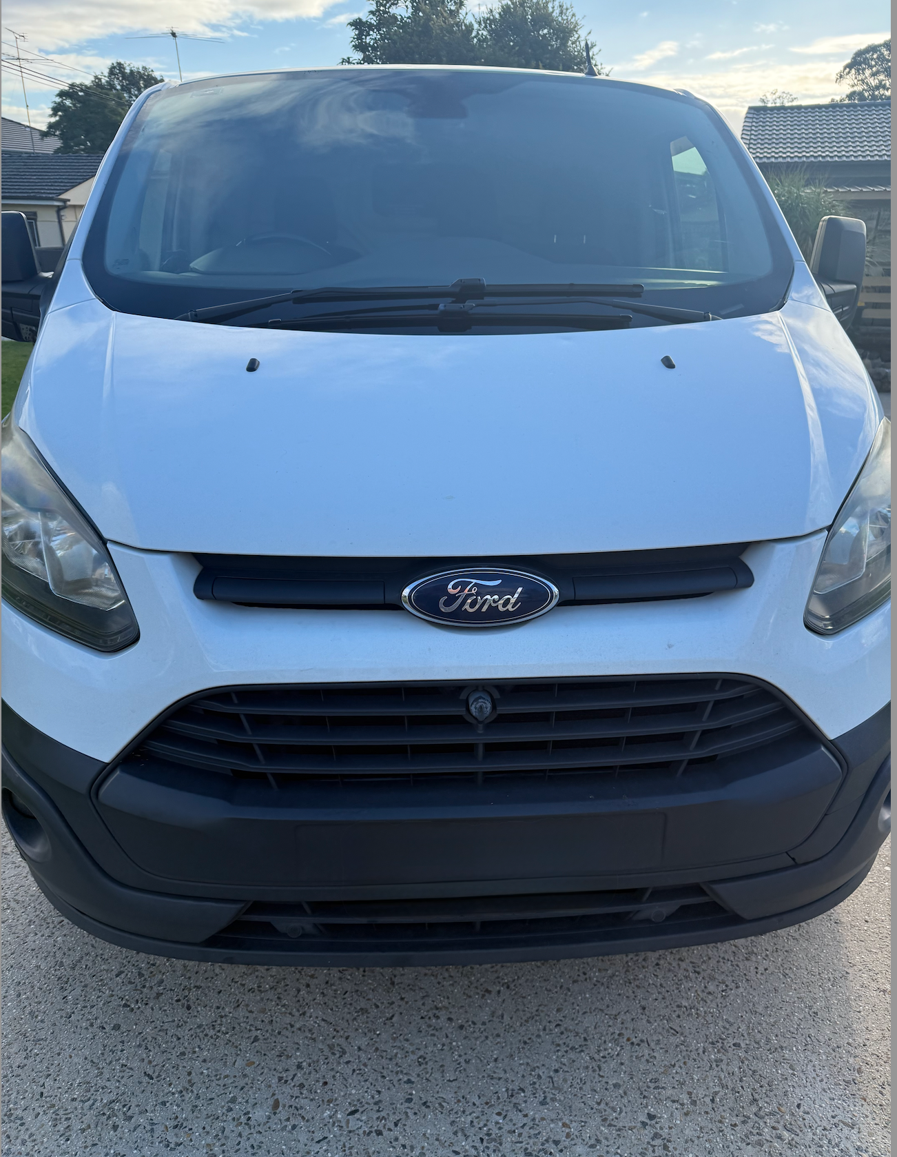 A white Ford Transit van, front-facing view, parked on a paved surface during the day.