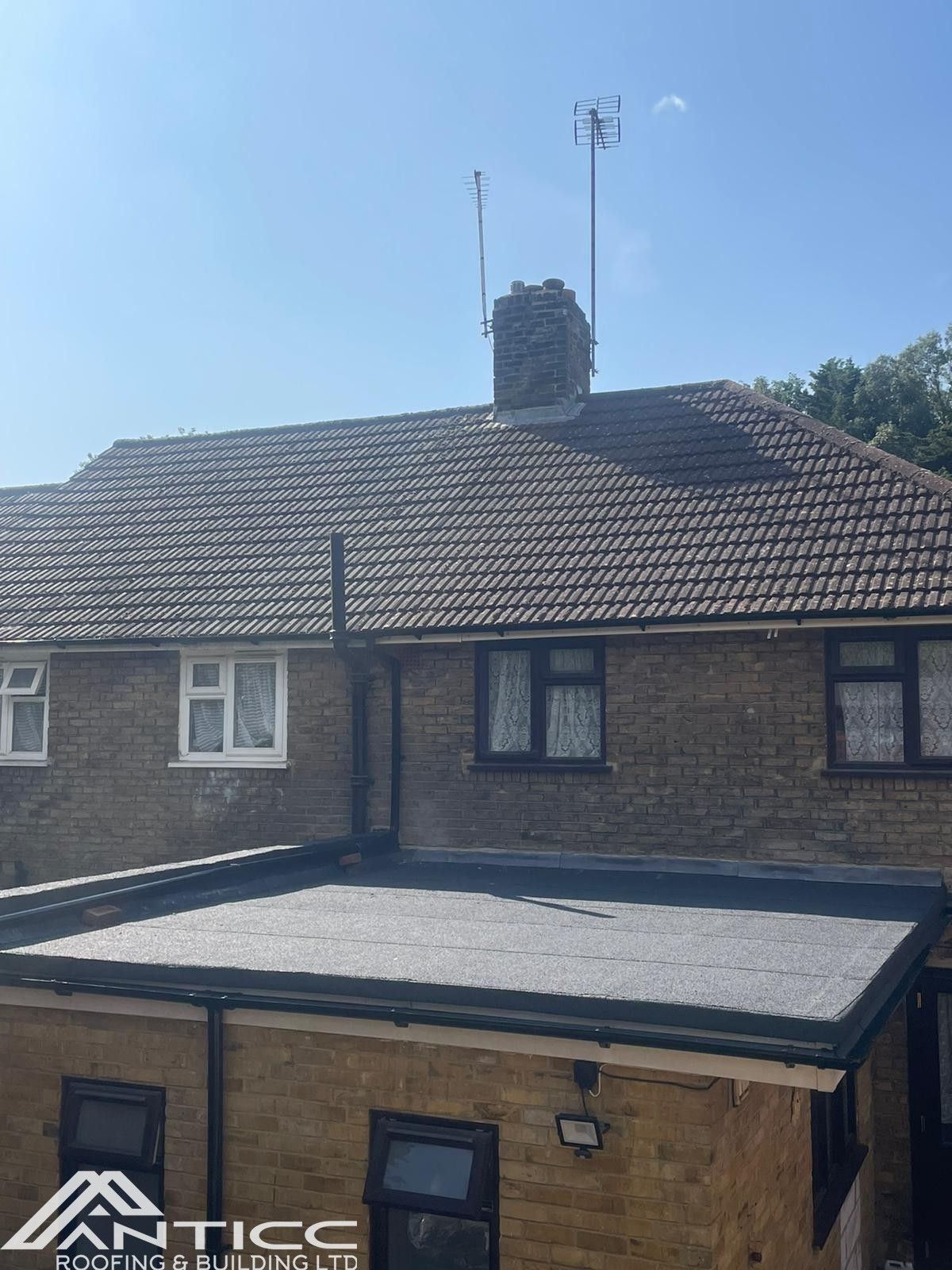 Brick house with tiled roof, chimney, and antenna under a clear blue sky